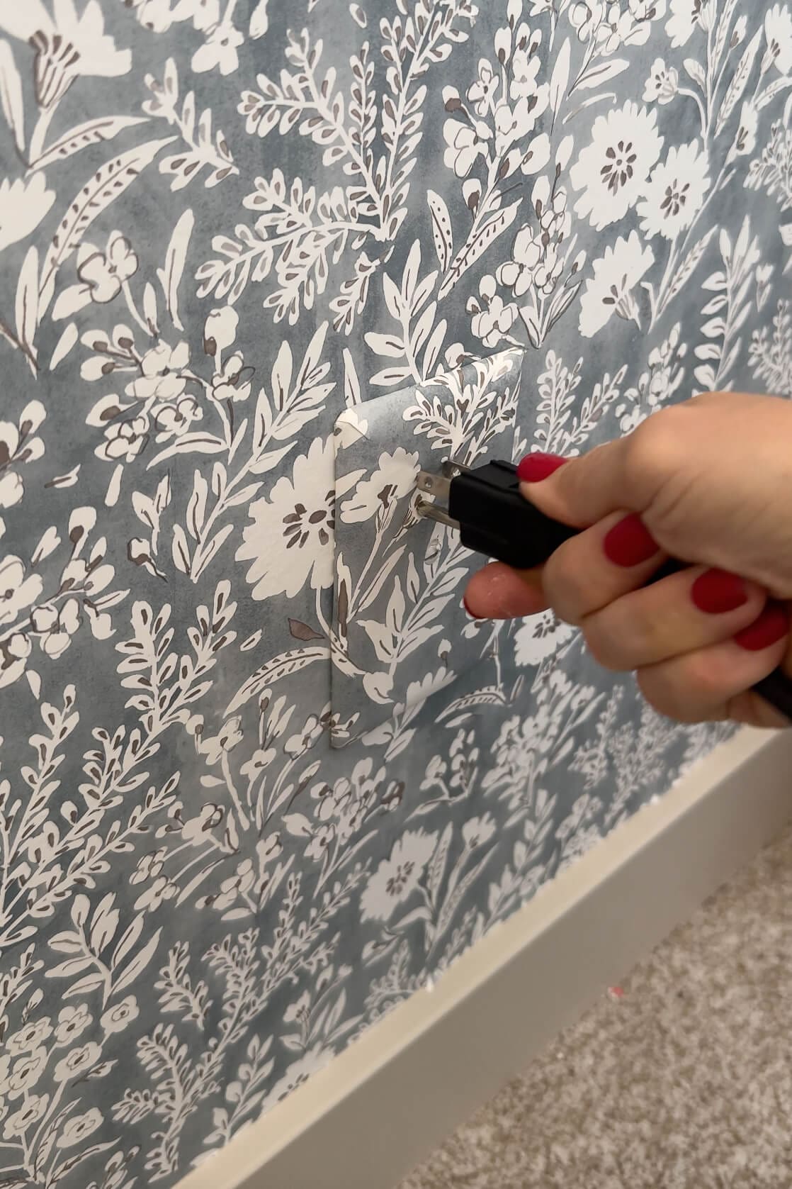 An electrical cord being plugged into a camouflaged outlet cover that blends perfectly into the wallpaper, creating a hidden outlet effect.