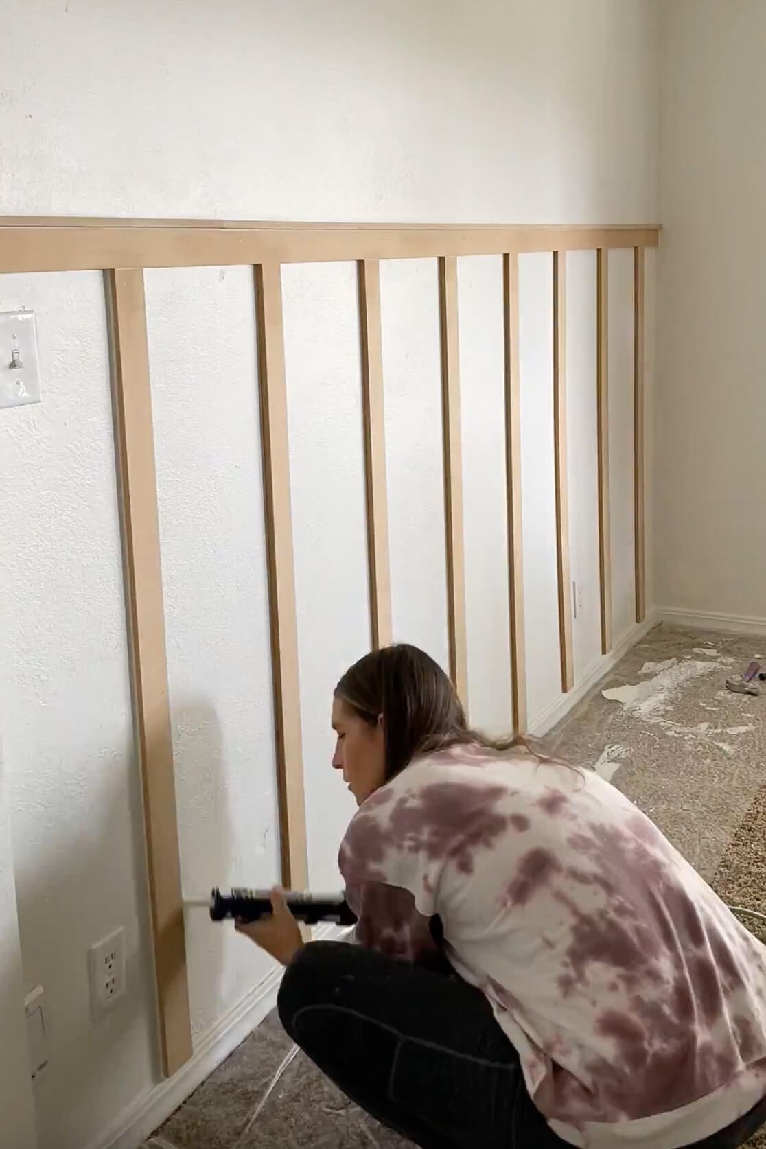 Applying caulk along the seams of vertical battens to prep for painting a clean and polished accent wall.