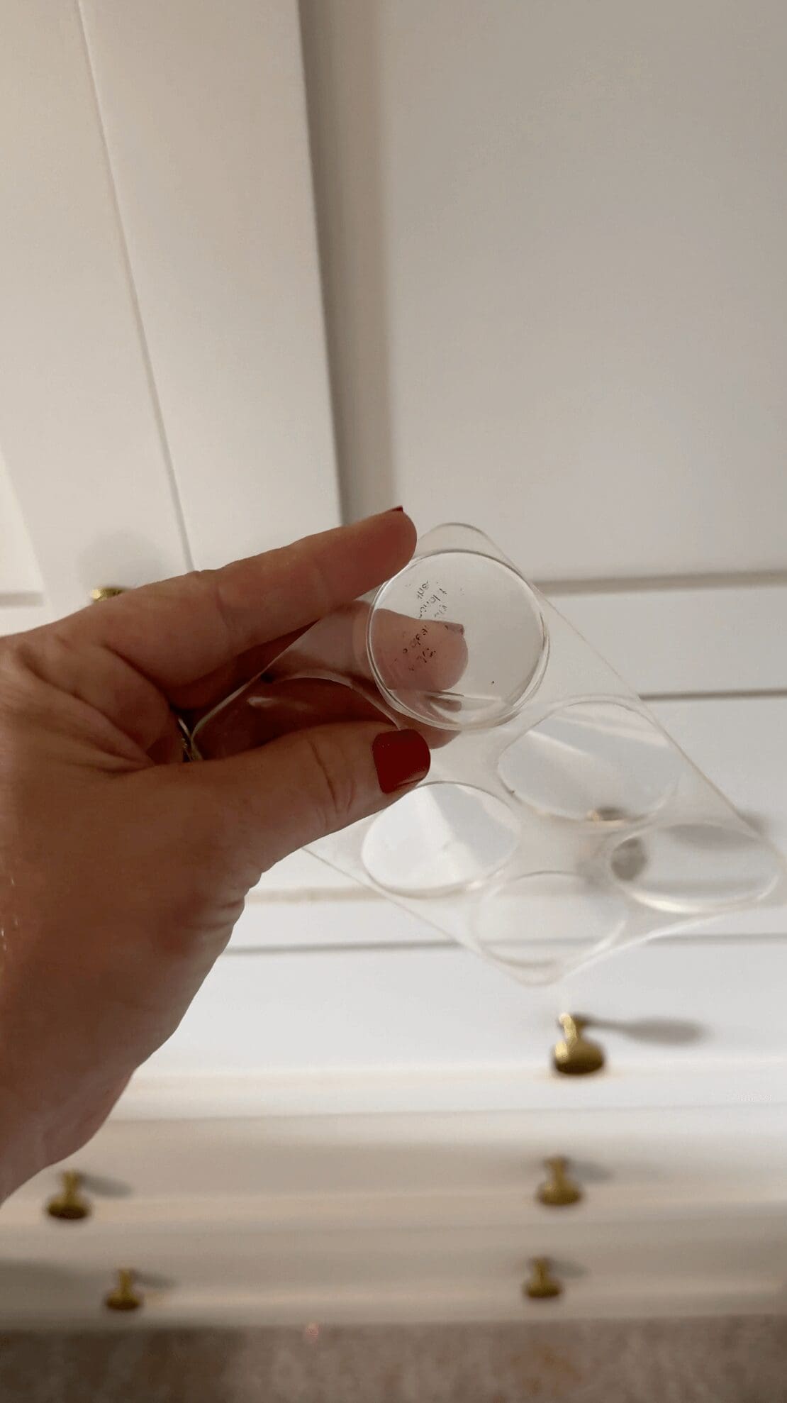 Hand holding a clear adhesive bumper designed to protect wallpaper from cabinet knobs or door handles.