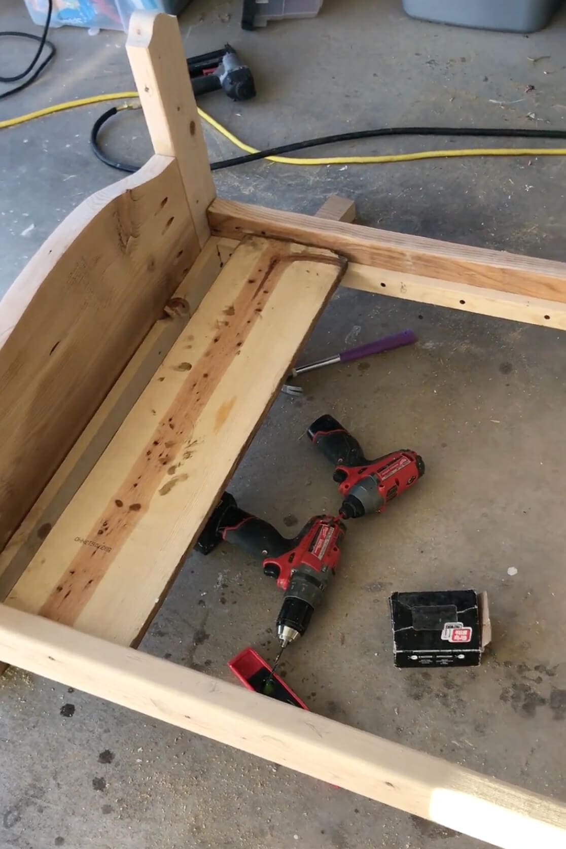 Bottom of the wooden bed frame showing scrap boards used for support, alongside drills and tools used in the assembly process.