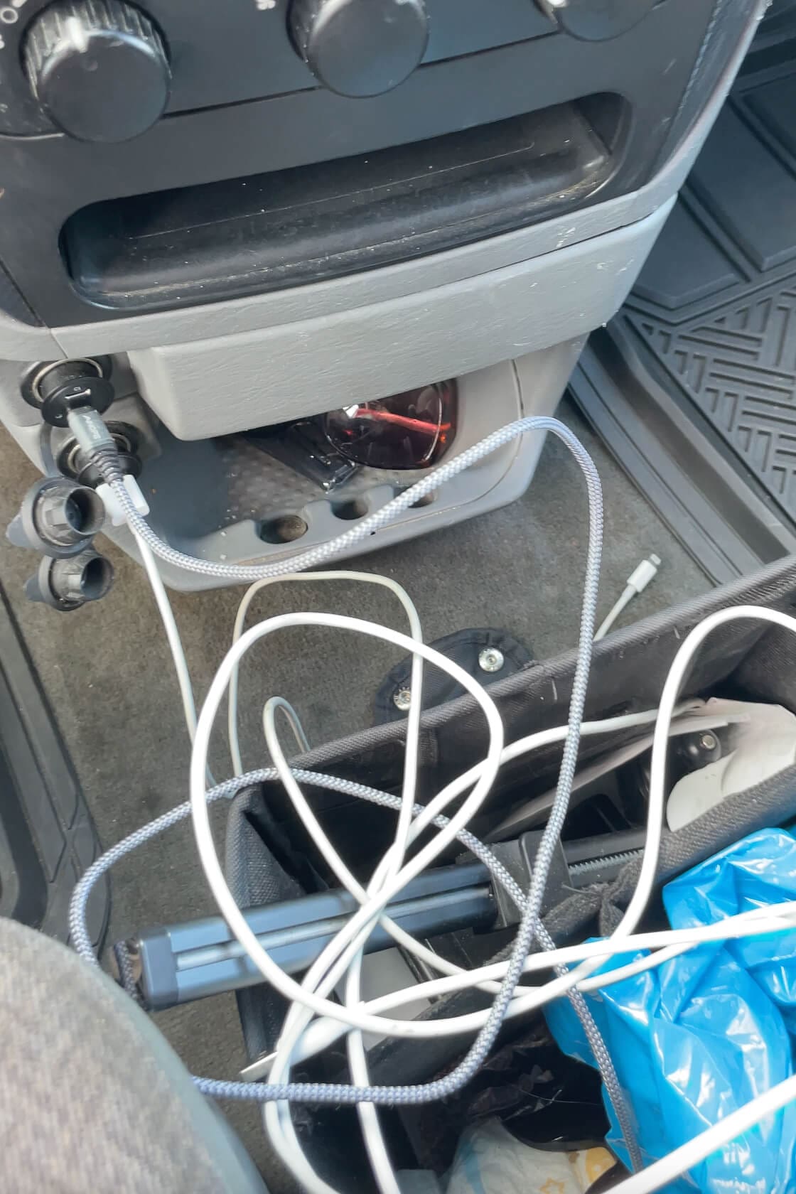 Tangle of phone cords and charging cables inside a car organizer on the floor near the center console, showing the reality of tech-packed road trips.