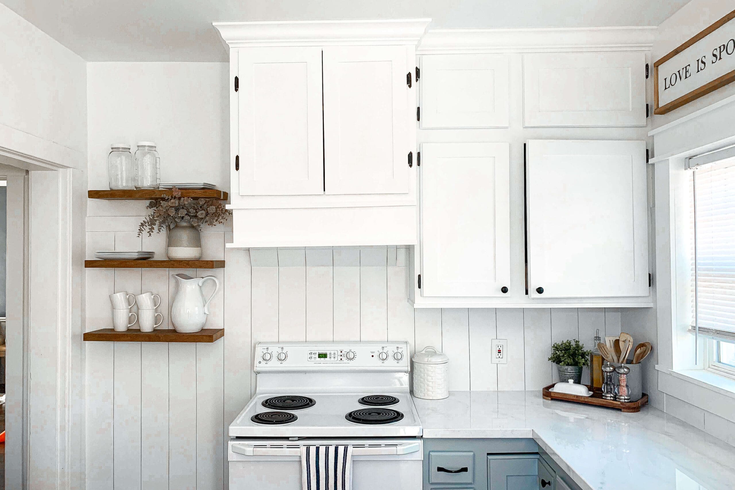 White kitchen corner with DIY floating shelves made from stained wood, styled with neutral dishes, glass jars, and dried florals, showcasing a budget-friendly open shelving solution.