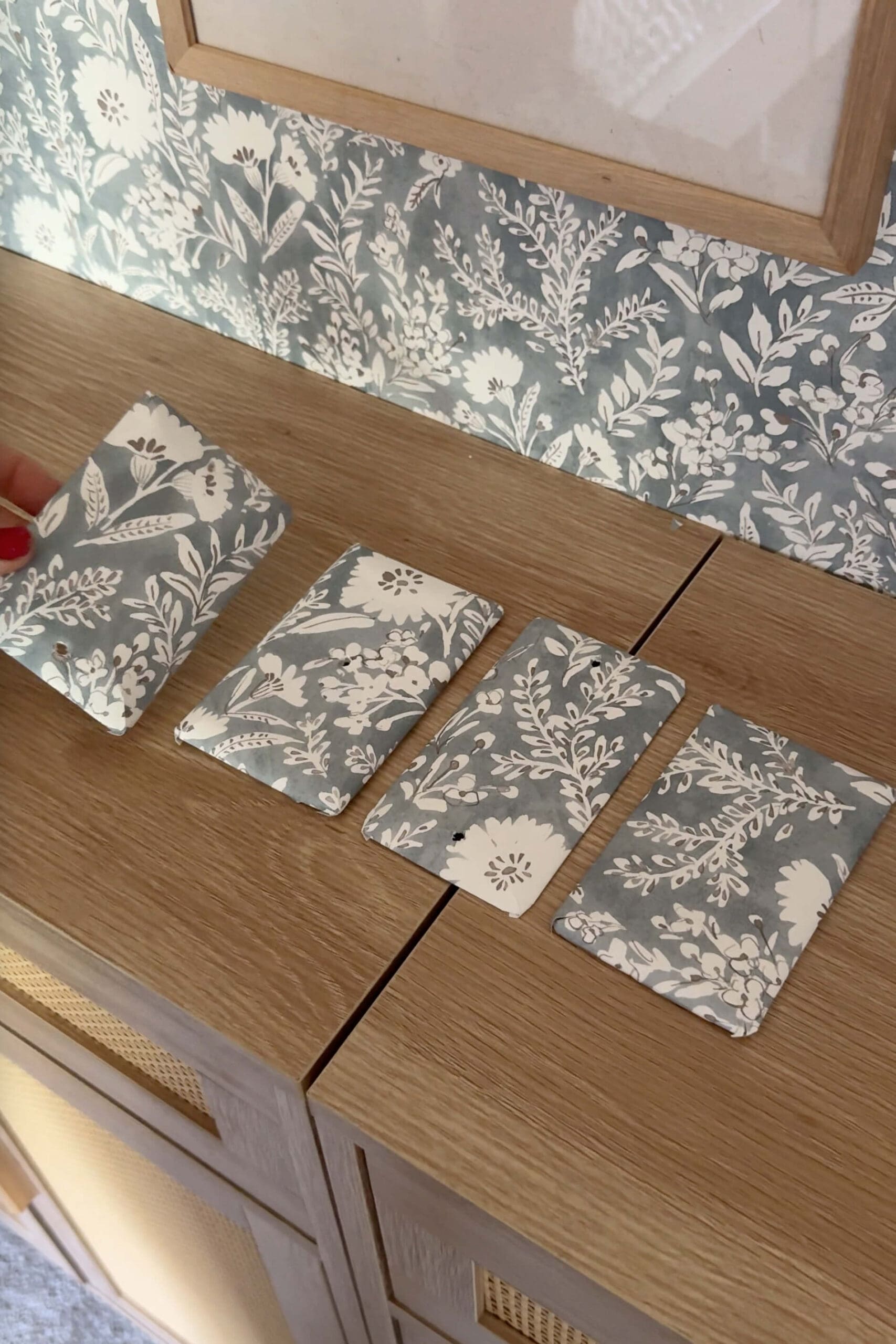 Floral wallpaper-wrapped outlet covers laid out on a wood cabinet, matching the wallpaper on the wall behind them.