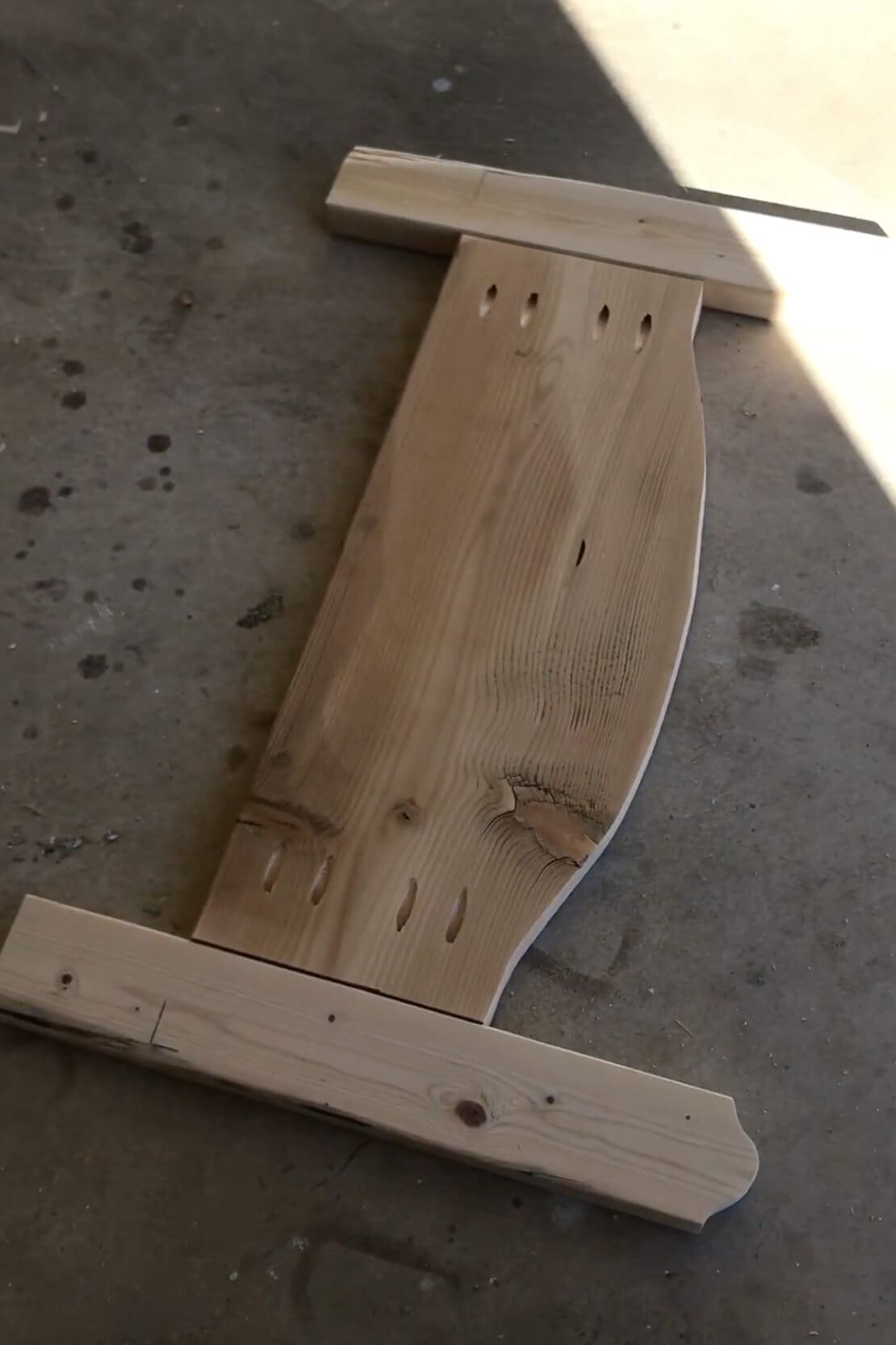 Close-up of pocket holes drilled into a curved wood panel, prepping for assembly of a handmade wooden bed.