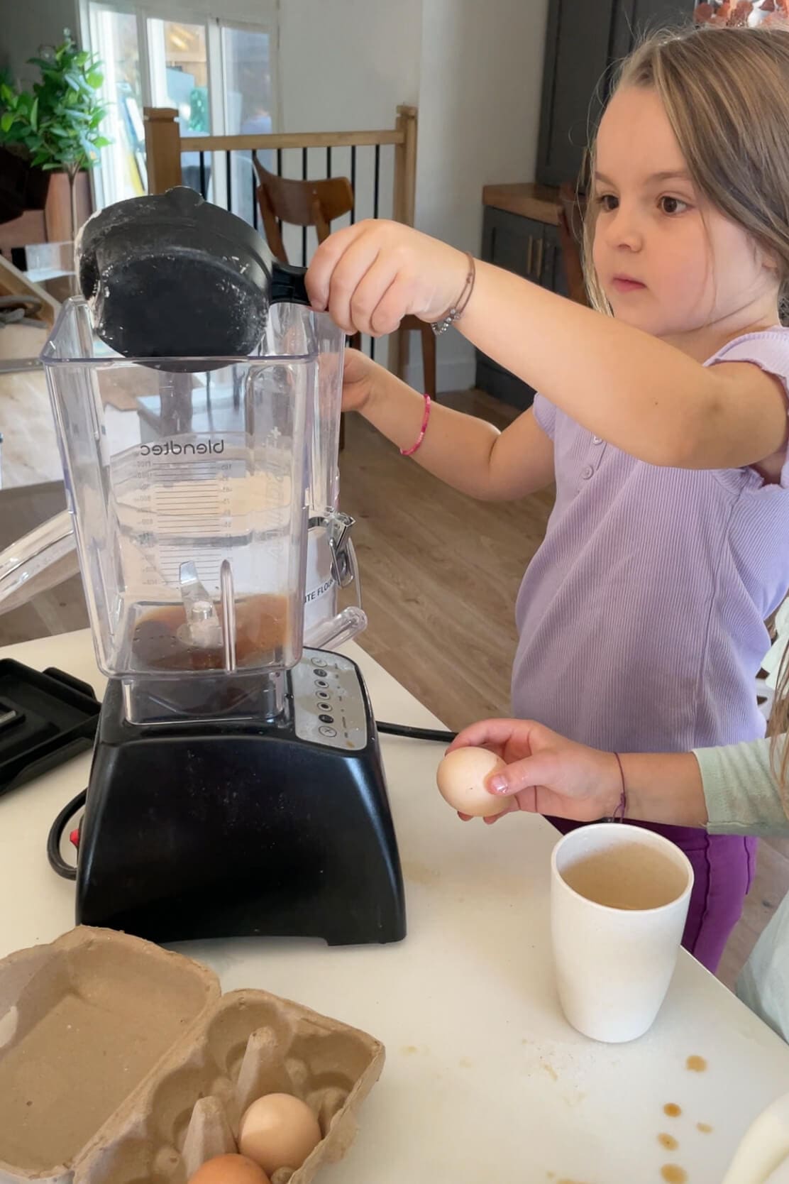 Child adding flour to a blender full of eggs and milk while prepping Dutch Baby batter in the kitchen.