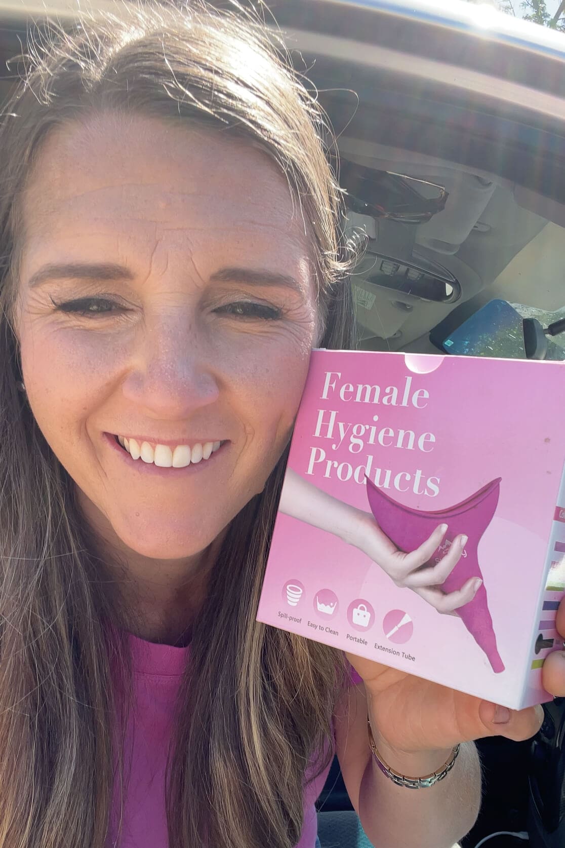 Woman smiling while holding a pink box labeled "Female Hygiene Products," sharing a helpful road trip essential for women.
