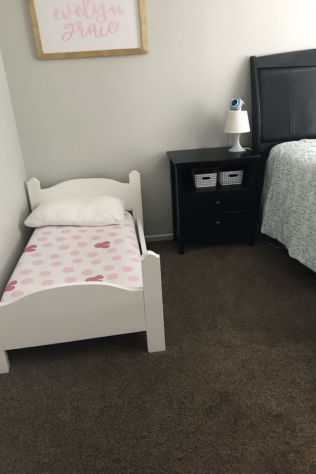 Finished DIY toddler bed painted white, styled in a shared bedroom setup with a nightstand and a larger bed nearby.