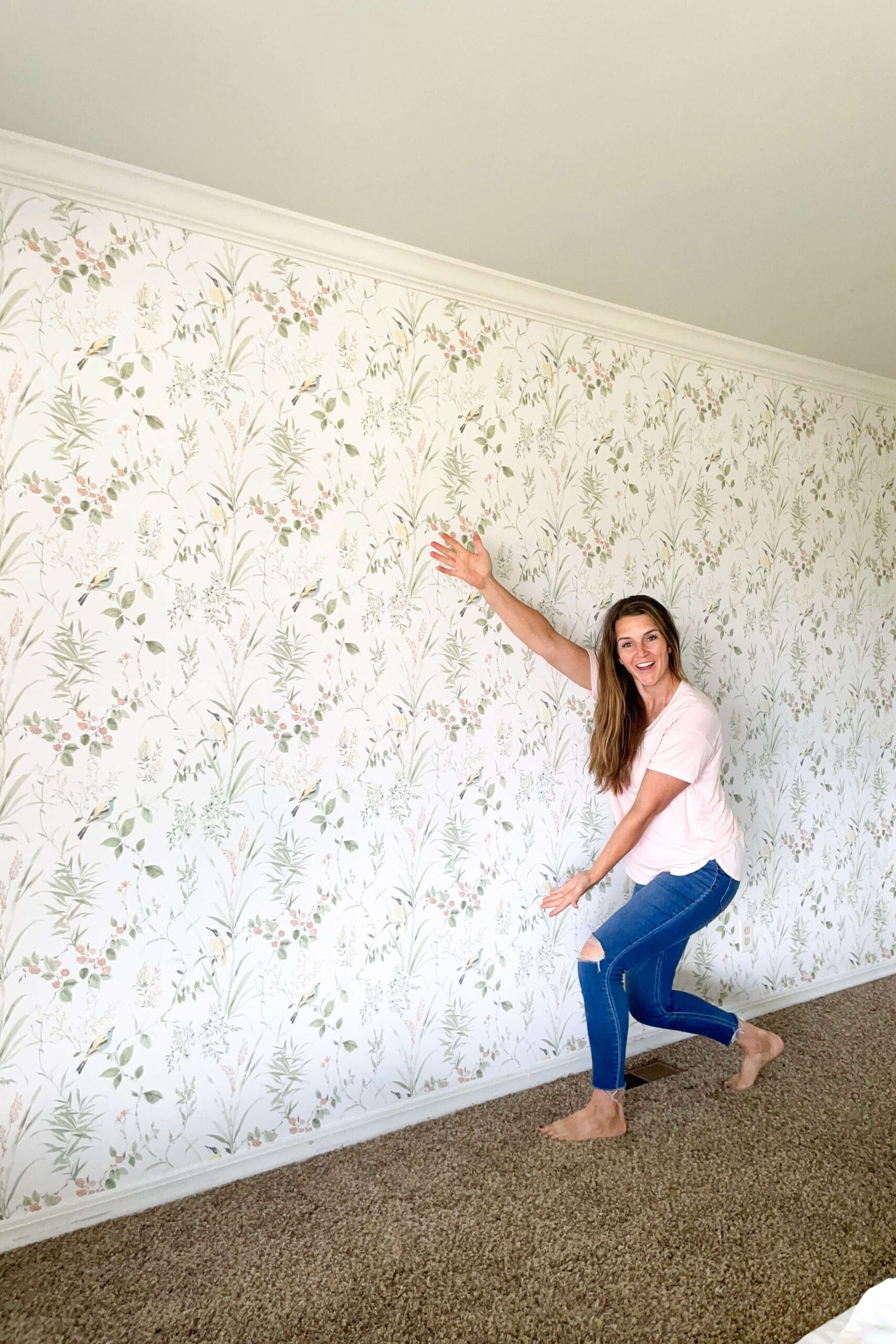 Smiling woman pointing to a freshly installed floral traditional wallpaper on a bedroom wall
