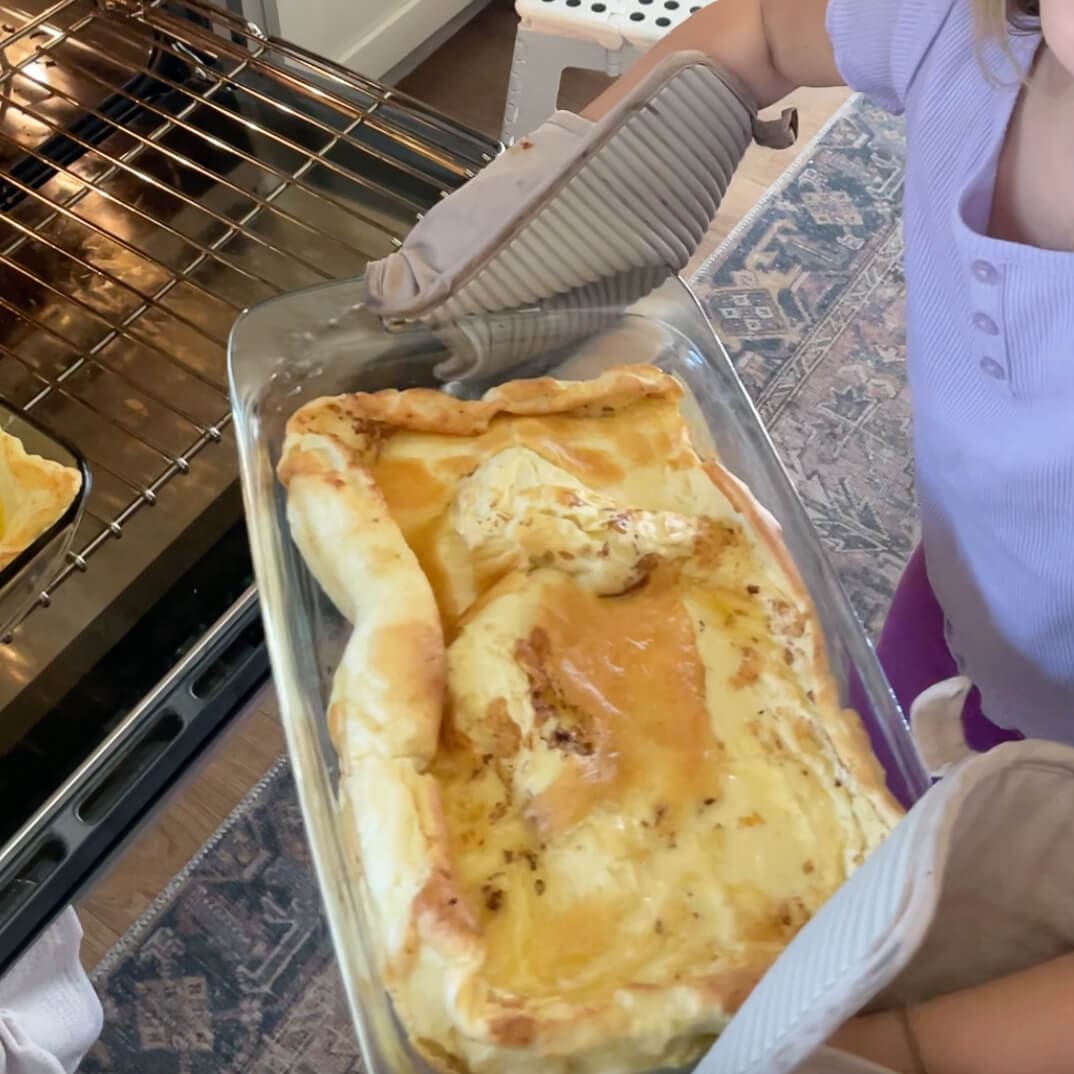 Child proudly holding a hot glass dish with a freshly baked German Pancake straight from the oven.