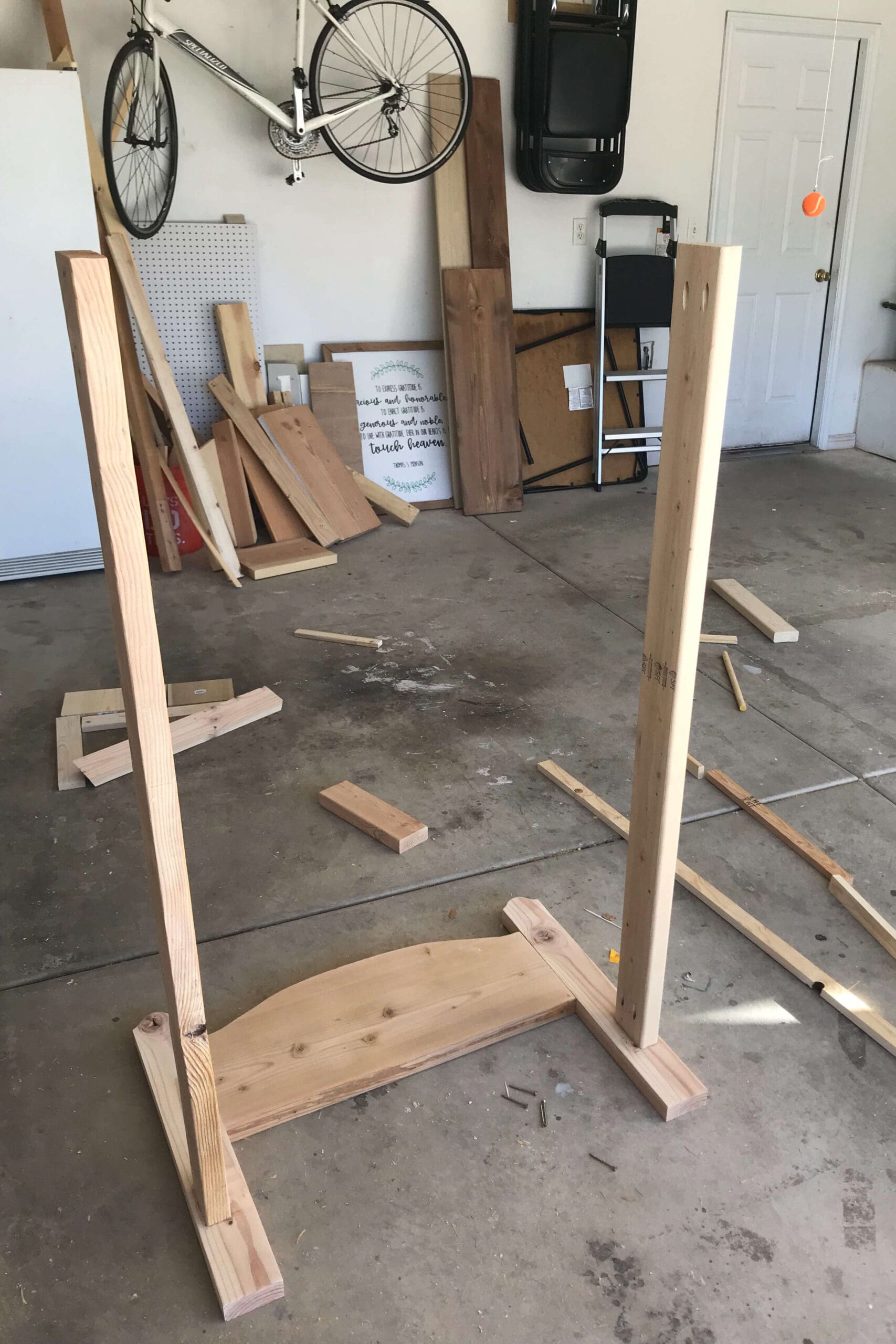 Wooden headboard panel standing upright with legs attached as part of assembling a homemade kids bed from scrap wood.
