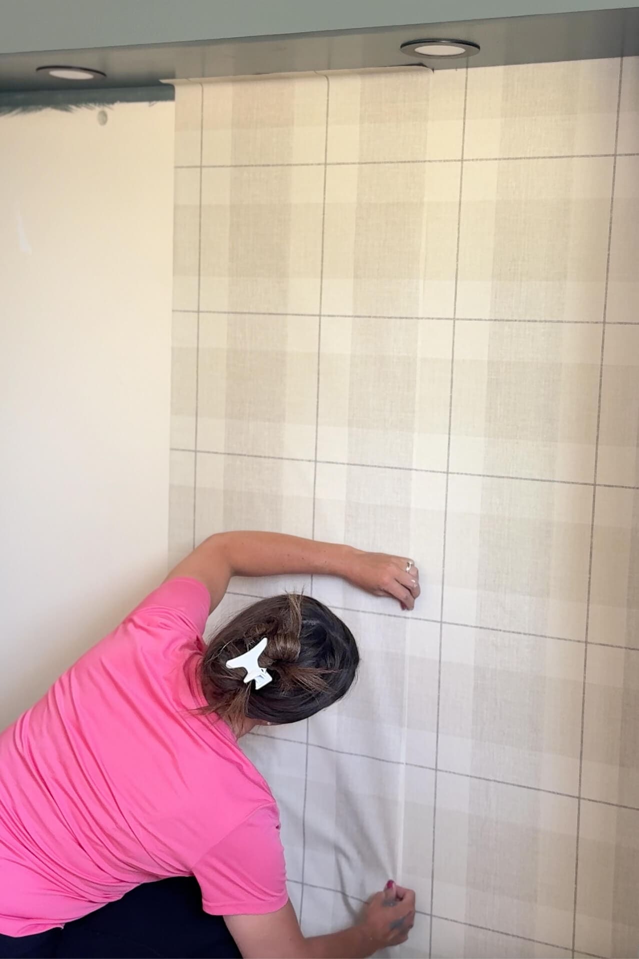 Matching seams and smoothing bubbles while installing plaid peel and stick wallpaper on a feature wall.