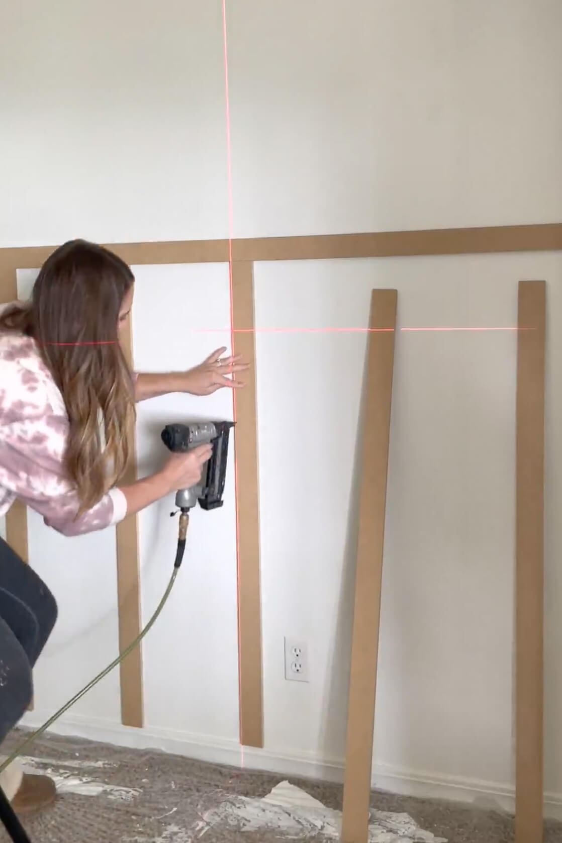 Aligning and nailing a vertical board into place with the help of a laser level during the board and batten wall build.