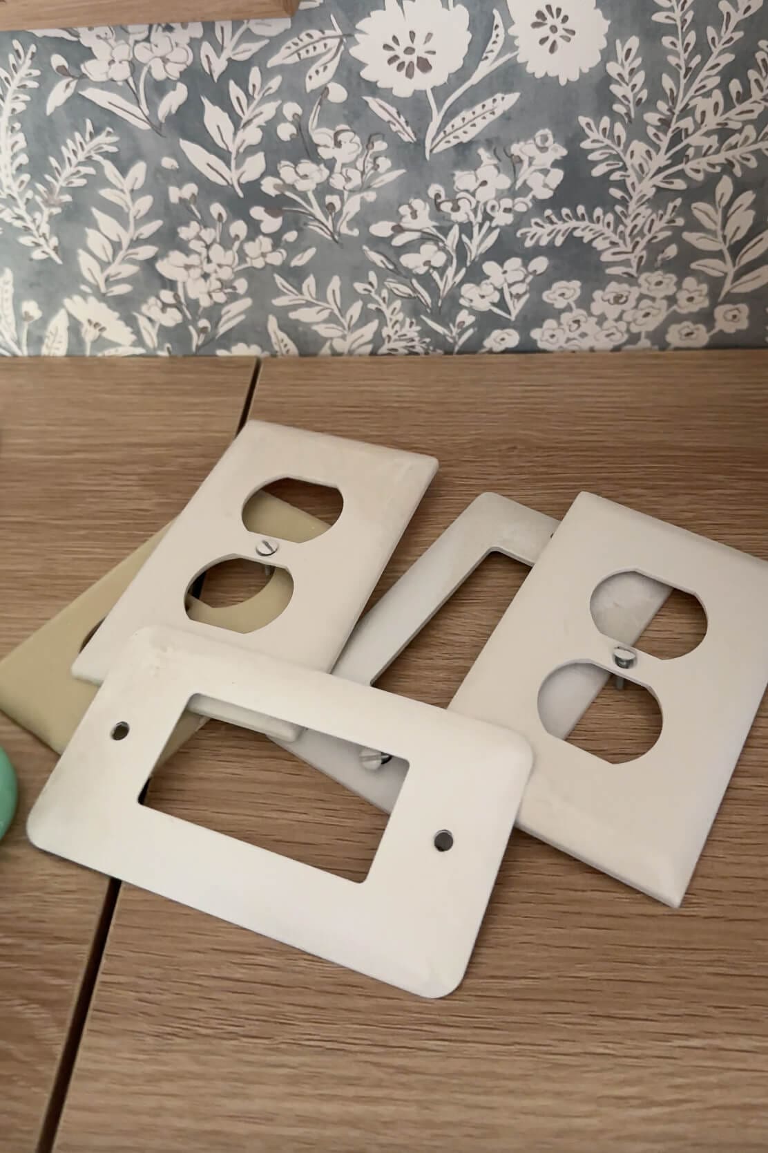 A pile of plain white and beige wall plates and switch plates laid out on a wood surface, ready for a DIY update.