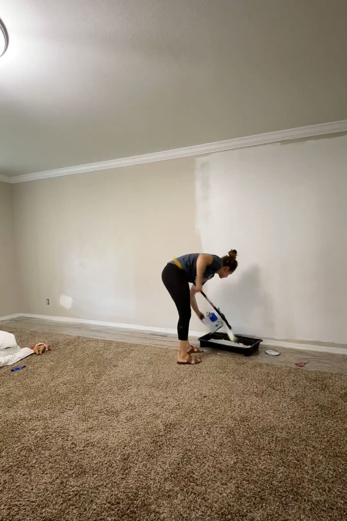 Woman loading a paint roller with white paint while prepping a bedroom wall