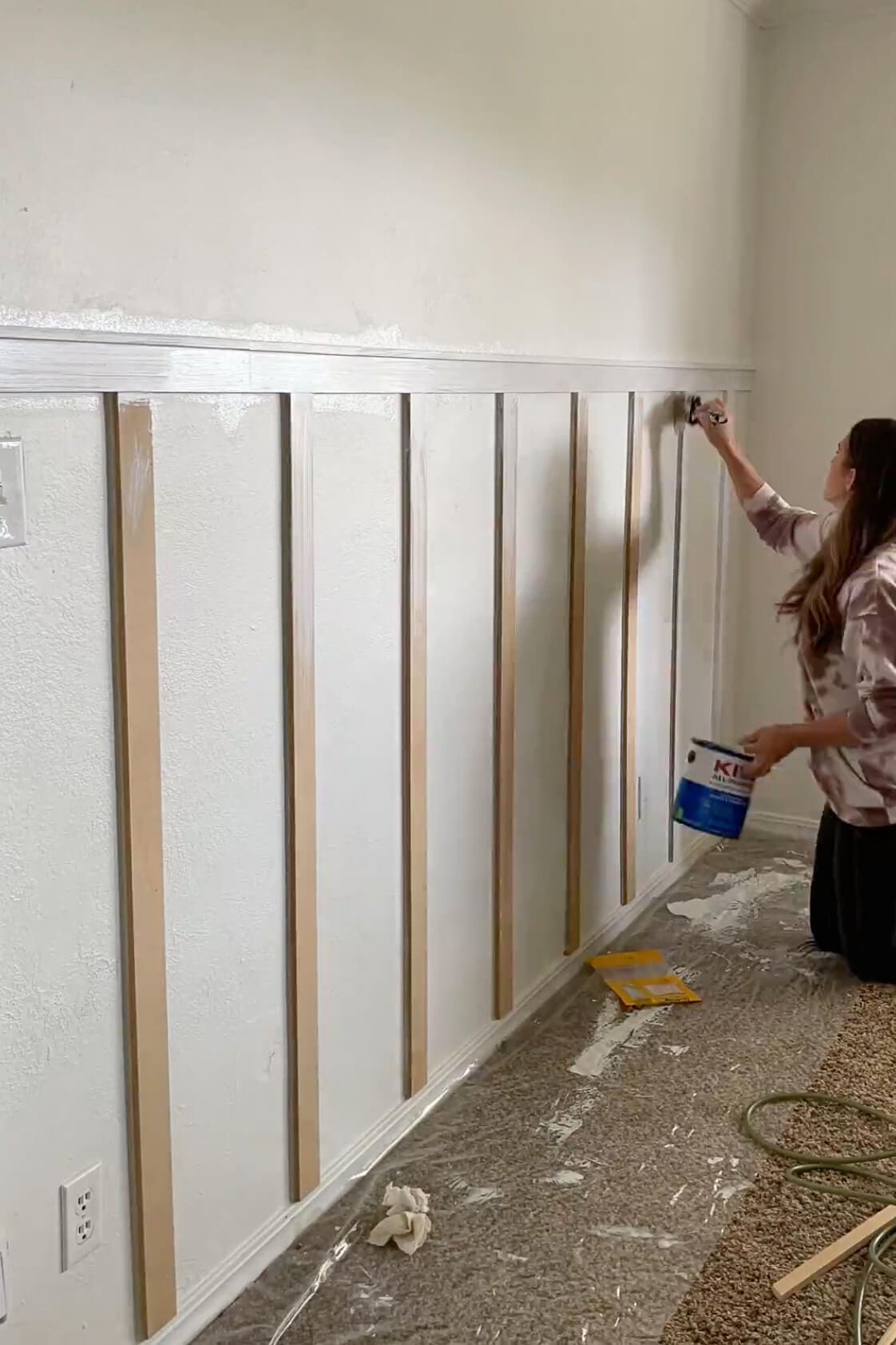 DIYer applying primer to the MDF trim with a brush before painting, prepping the feature wall for a smooth finish.