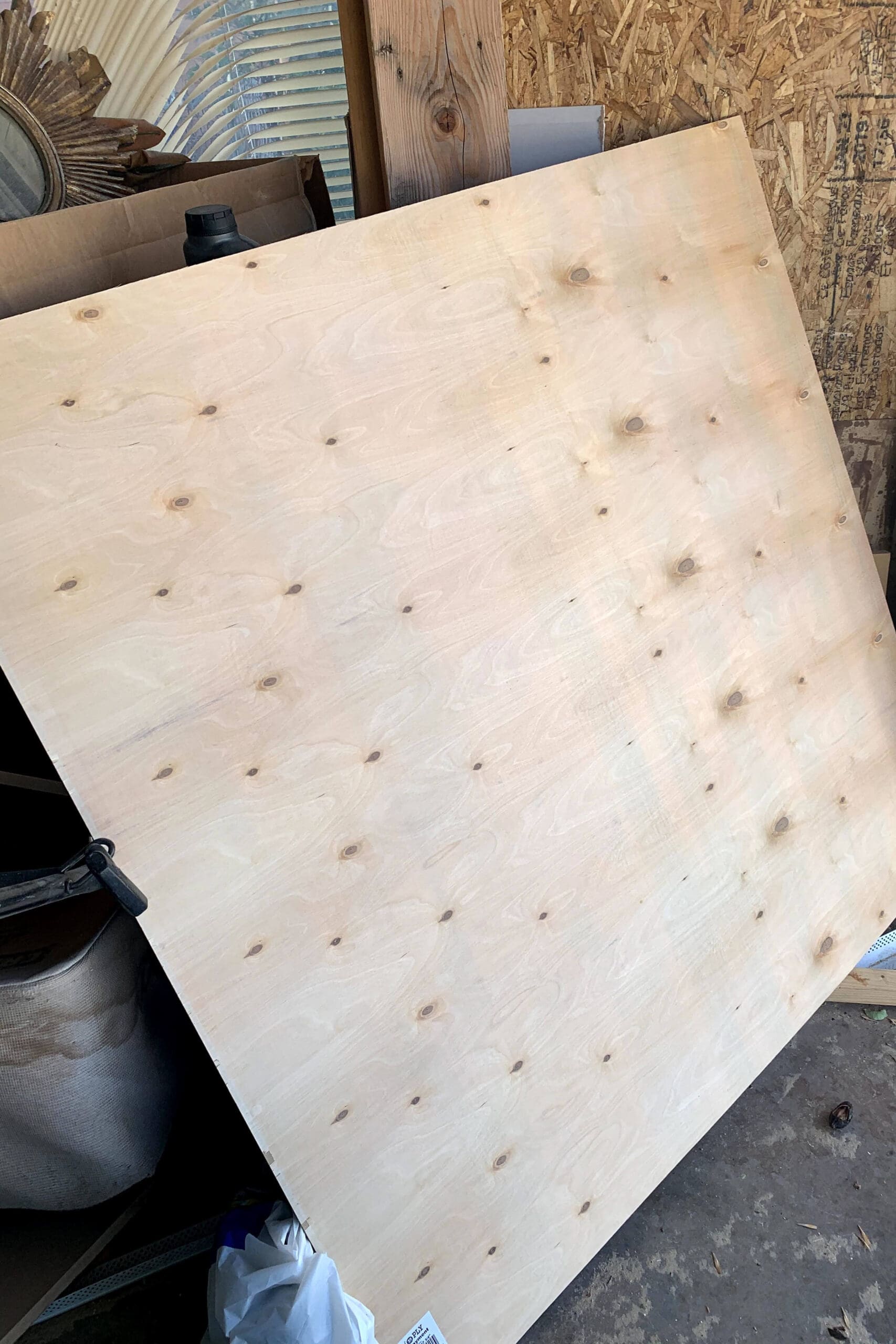 Full sheet of 1/4-inch plywood leaning against a workshop wall, ready to be cut down for a DIY floating shelf project using budget-friendly materials.