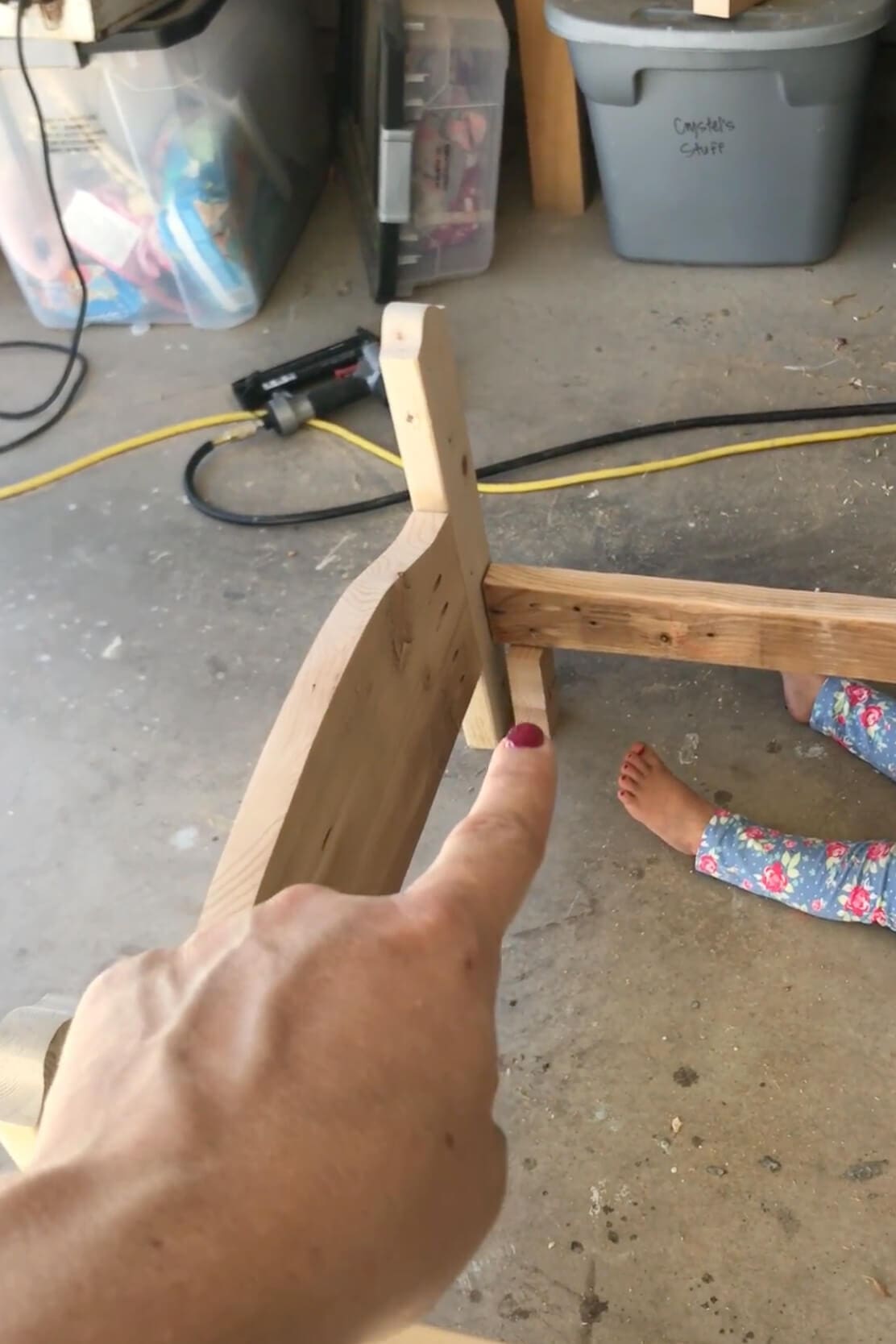 Close-up of a finger pointing to a joint where the bed rail meets the leg on a handmade wooden frame, built from scrap lumber.