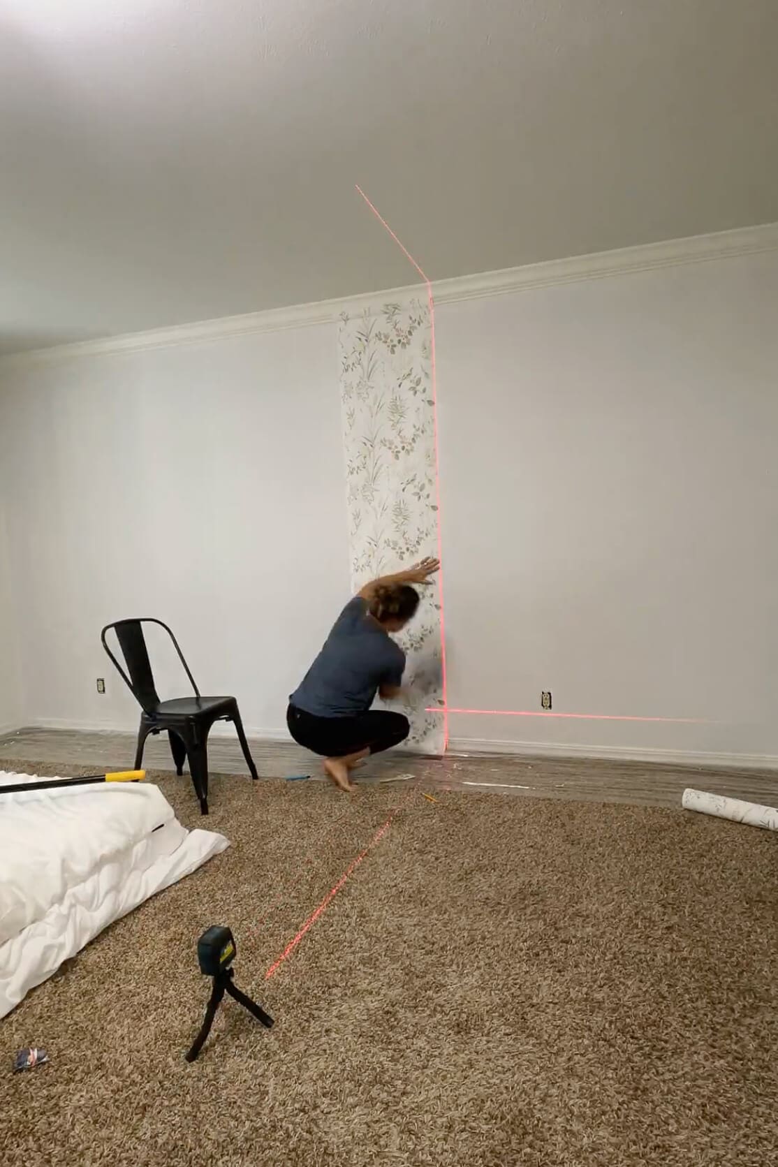 Smoothing a panel of traditional wallpaper onto the wall while using a laser level for precision