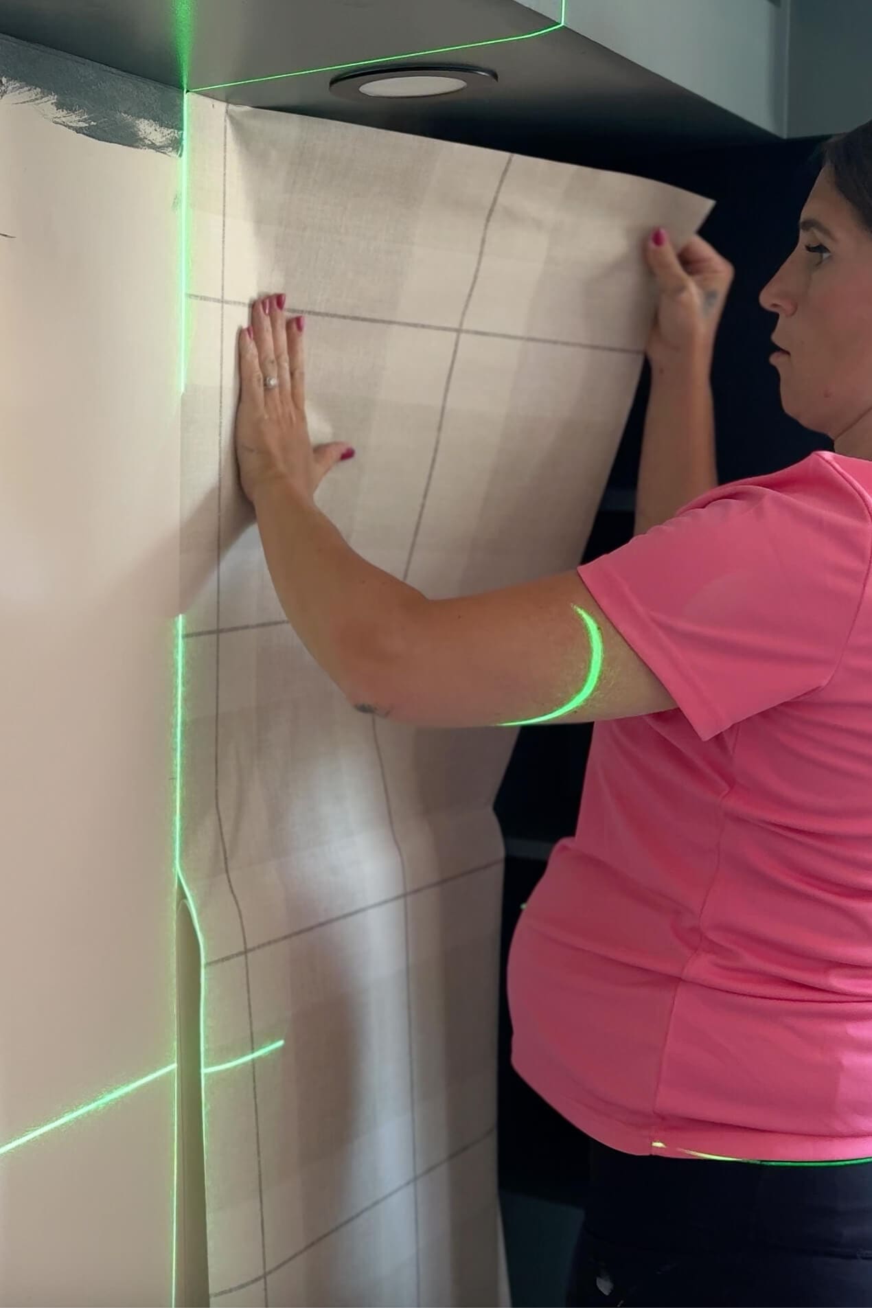 Smoothing plaid peel and stick wallpaper onto the wall, carefully following a vertical laser guide.