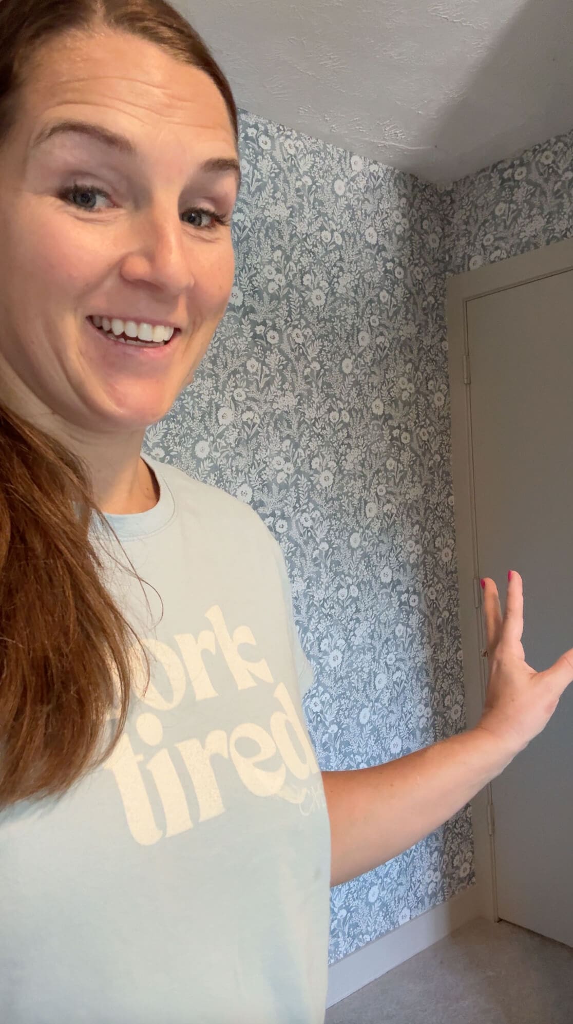 Smiling woman in front of a freshly finished wall, showing the finished result of her DIY floral wall project.
