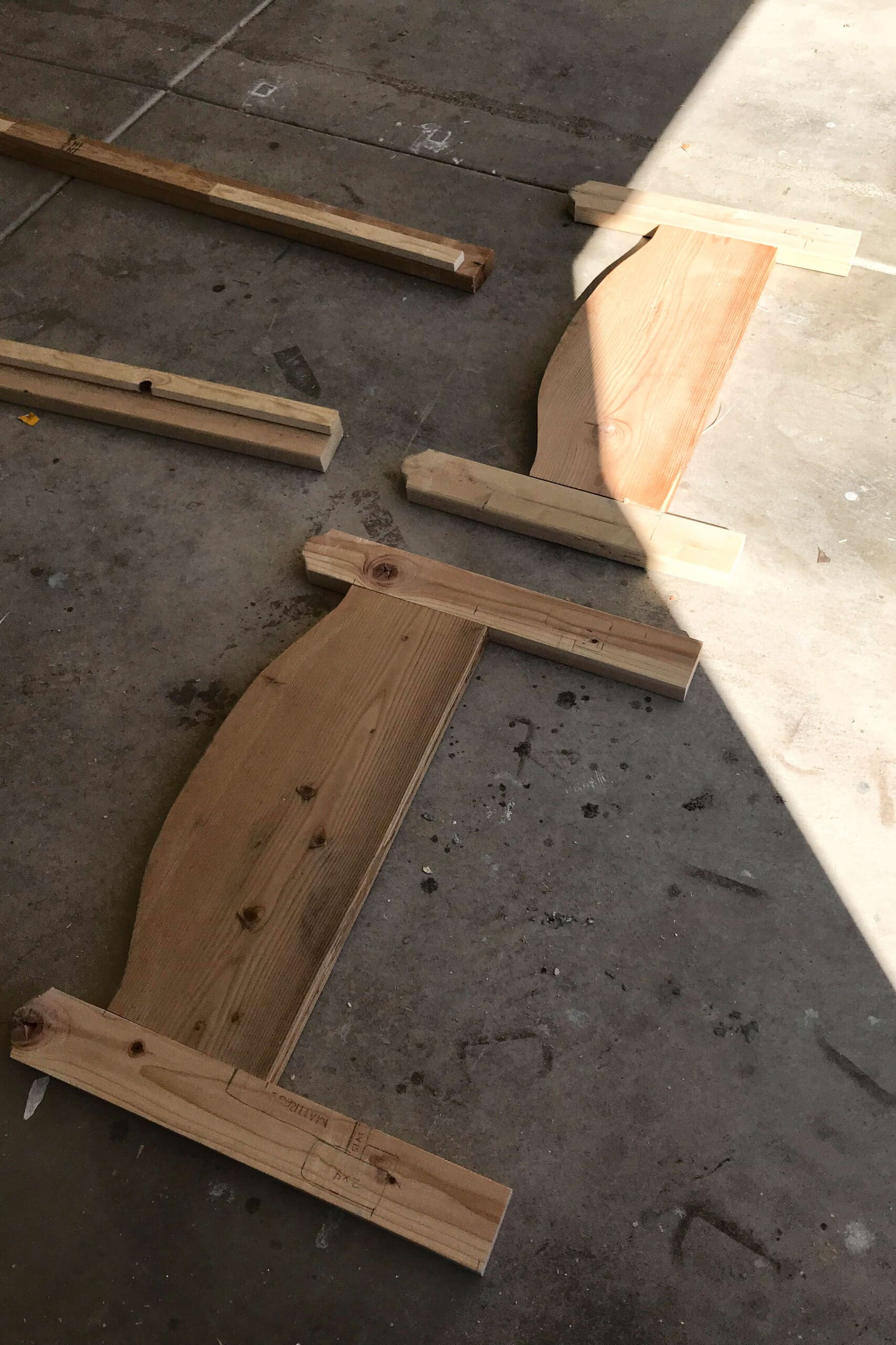 Headboard and footboard panels laid out on a garage floor while planning the frame for a wooden kids bed.