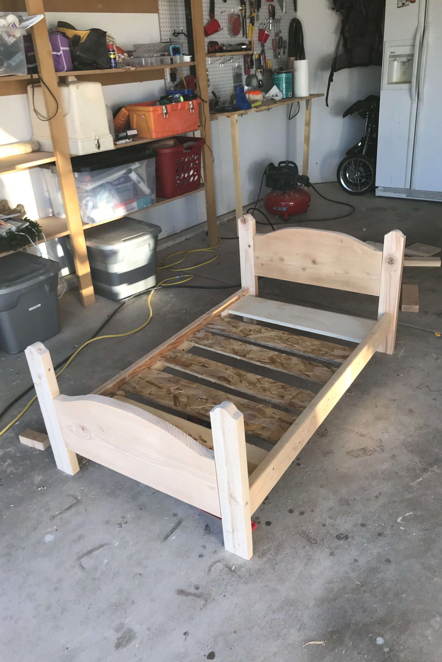DIY wooden bed frame fully assembled with support slats installed, built in a home garage workshop.