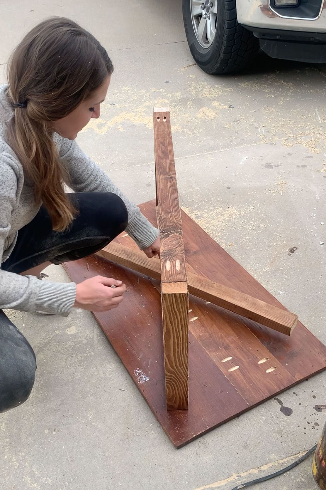 Positioning and marking placement of stained wooden legs on the underside of a repurposed wood tabletop for a DIY coffee table.