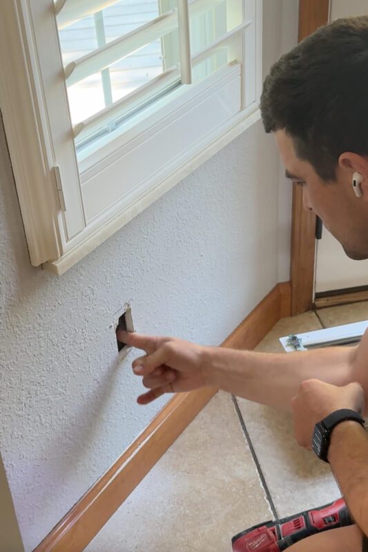 Man inspecting the inside of a wall after making a test cut before cutting a larger hole in the drywall.