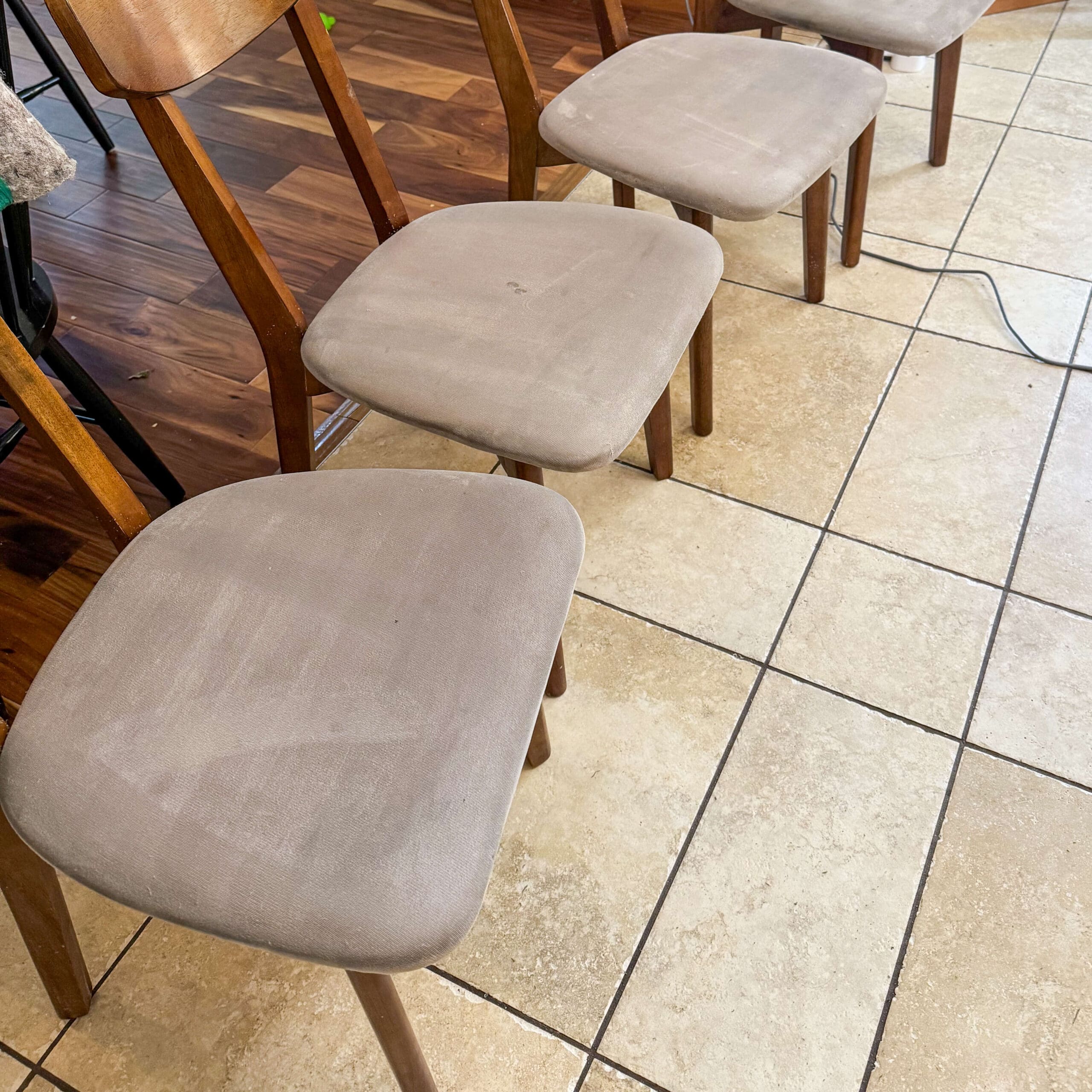 Freshly cleaned fabric dining chairs with light beige upholstery, neatly lined up on tile floor after deep cleaning.