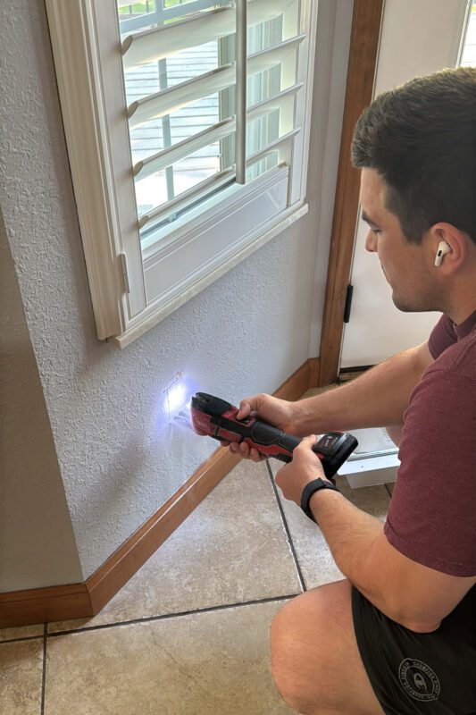 Man using a Milwaukee oscillating multi-tool to cut a hole in the drywall. 