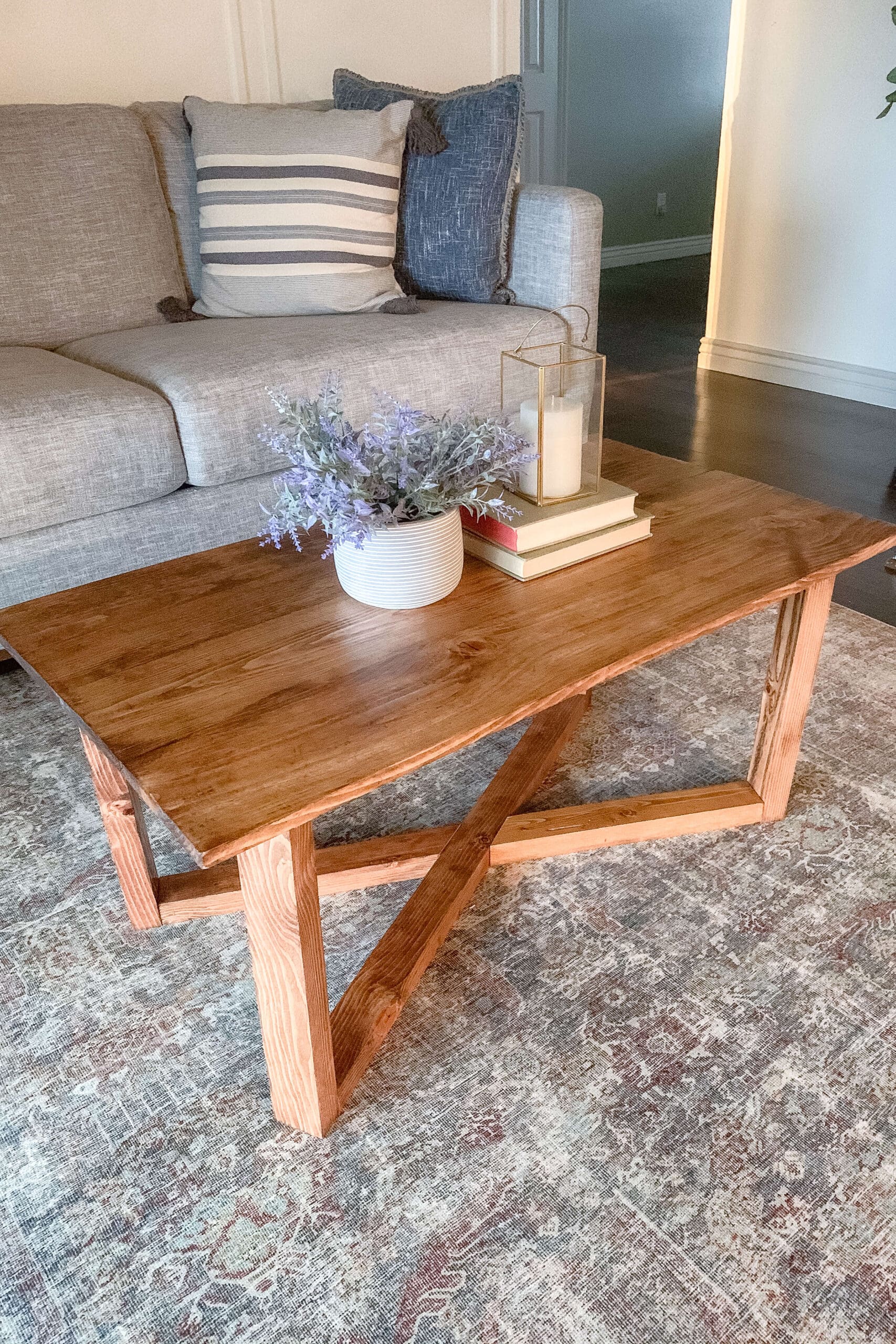 Close-up of a DIY coffee table made from repurposed wood, with decorative books, a gold lantern, and lavender in a white vase on top.