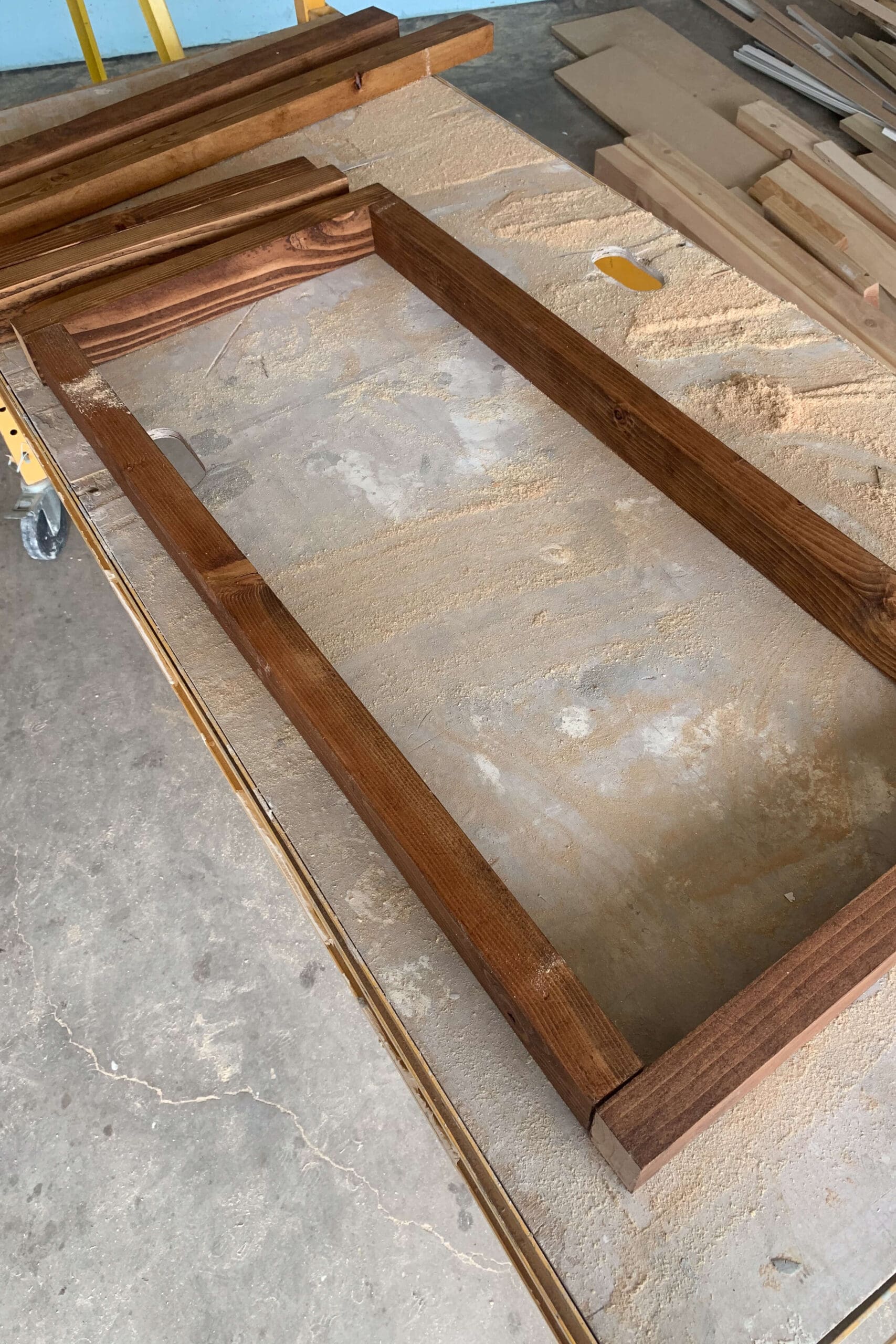 Freshly stained rectangular wood frame for a DIY coffee table, laid out on a workshop surface with sawdust.