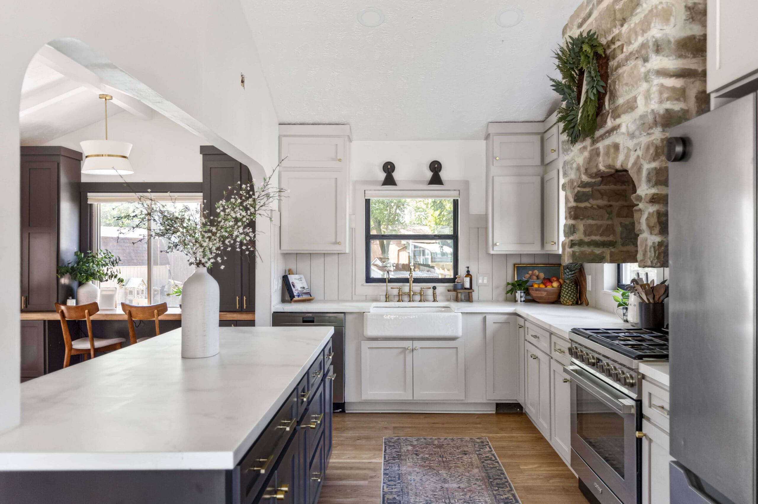 Epoxy kitchen countertops with faux marble finish on a dark island and white perimeter cabinets, featuring a farmhouse sink, gold faucet, and stone range hood