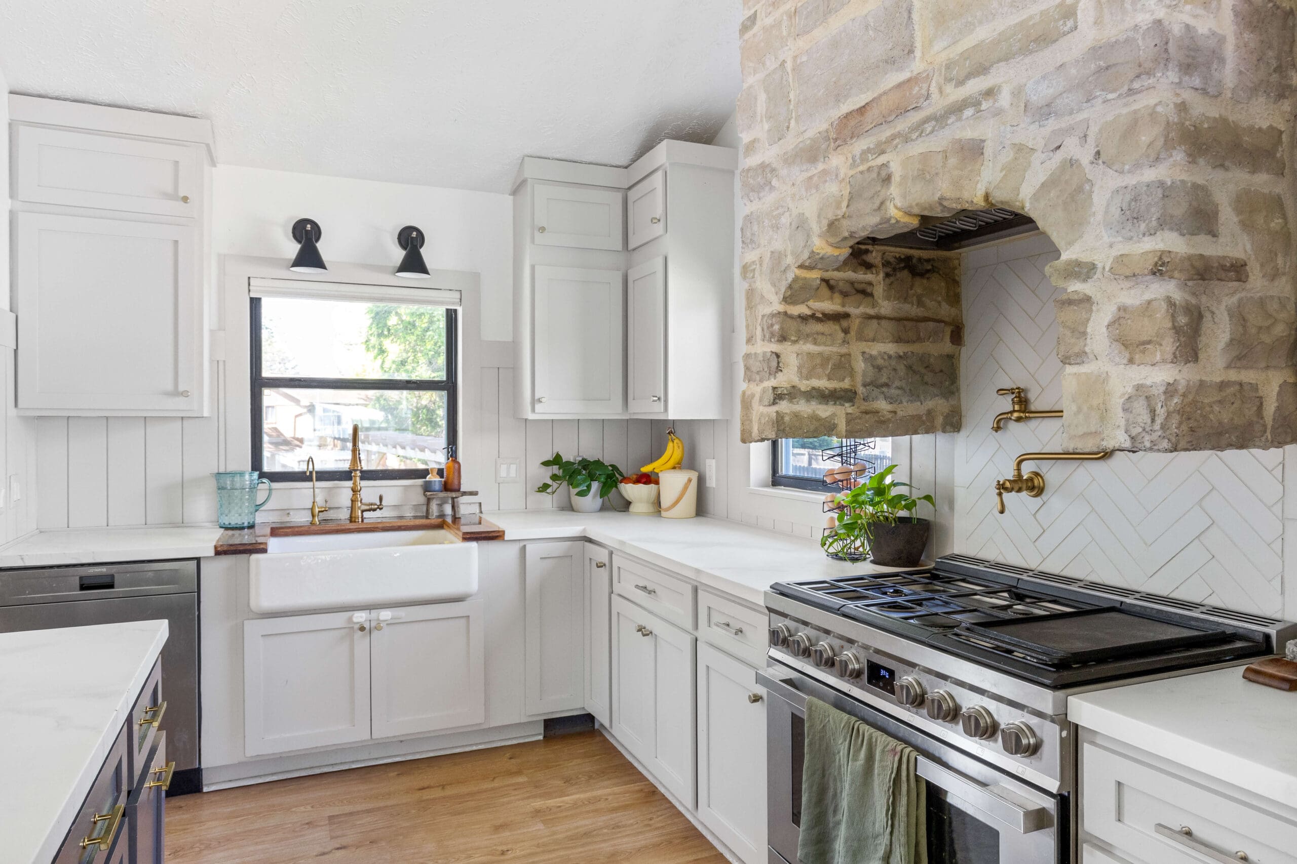 Close-up of epoxy kitchen countertops with faux marble finish, white shaker cabinets, stone range hood, and gold pot filler above stainless steel stove