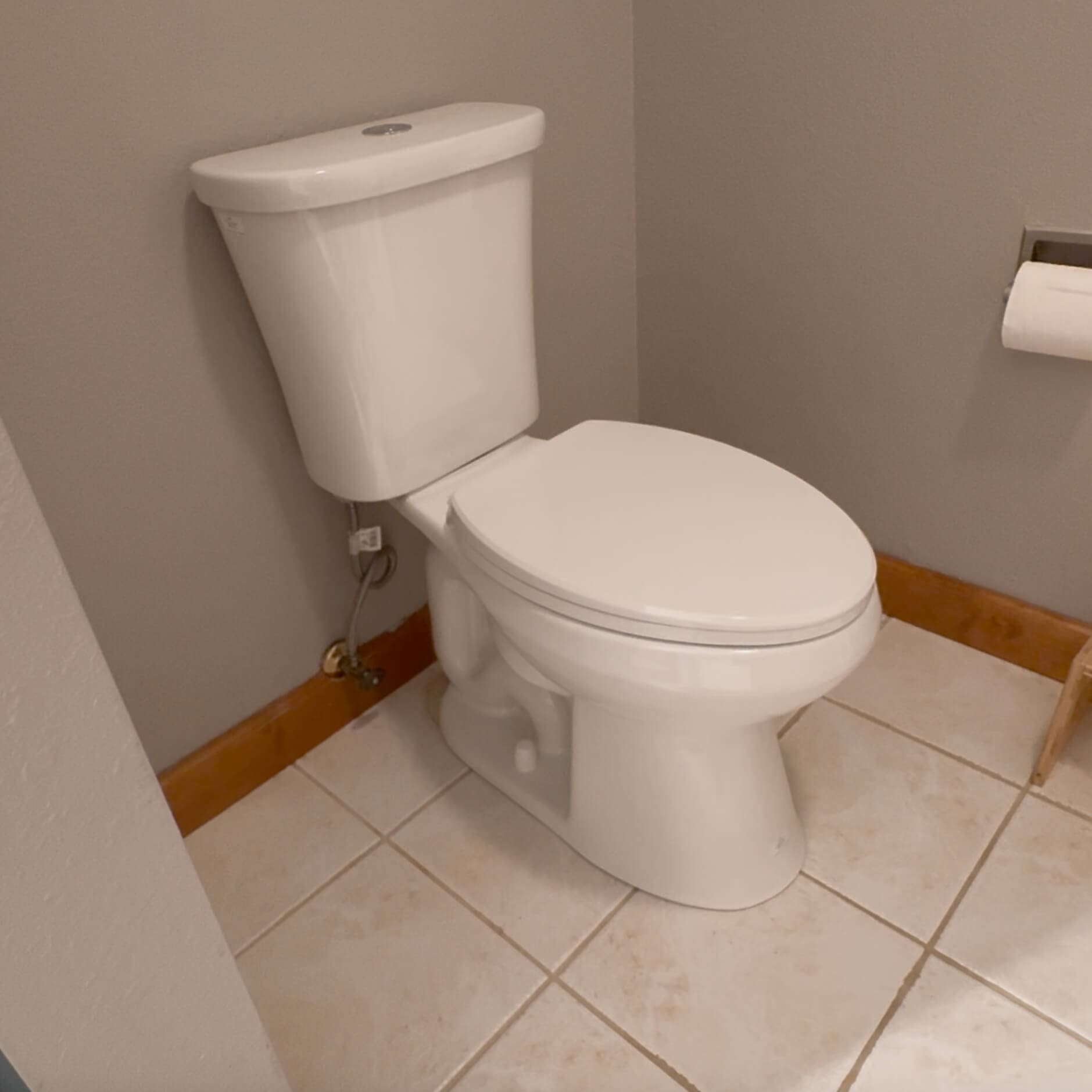 Close-up view of the new white toilet installed in the primary bathroom with fresh caulk and updated plumbing after replacing an old toilet.