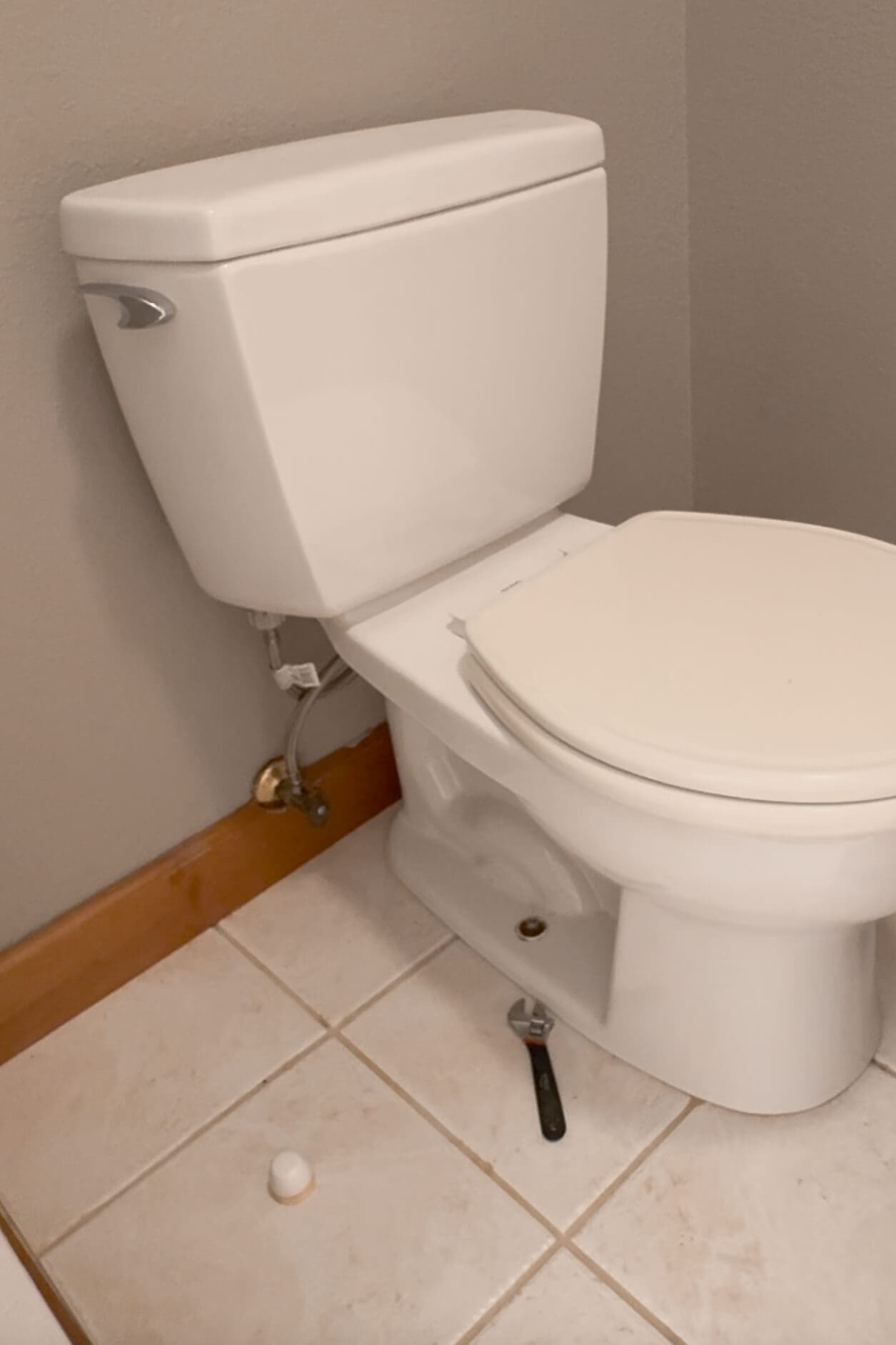 Old toilet partially disconnected with wrench on the floor, showing progress during a DIY project to replace a toilet in the primary bathroom.