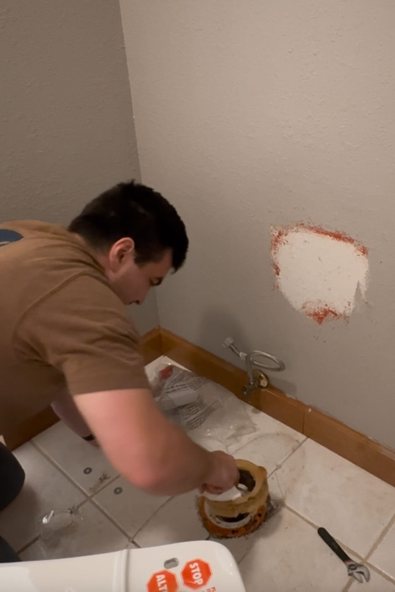 Man removing an old wax ring from the toilet flange during a DIY project to replace a toilet in the primary bathroom.