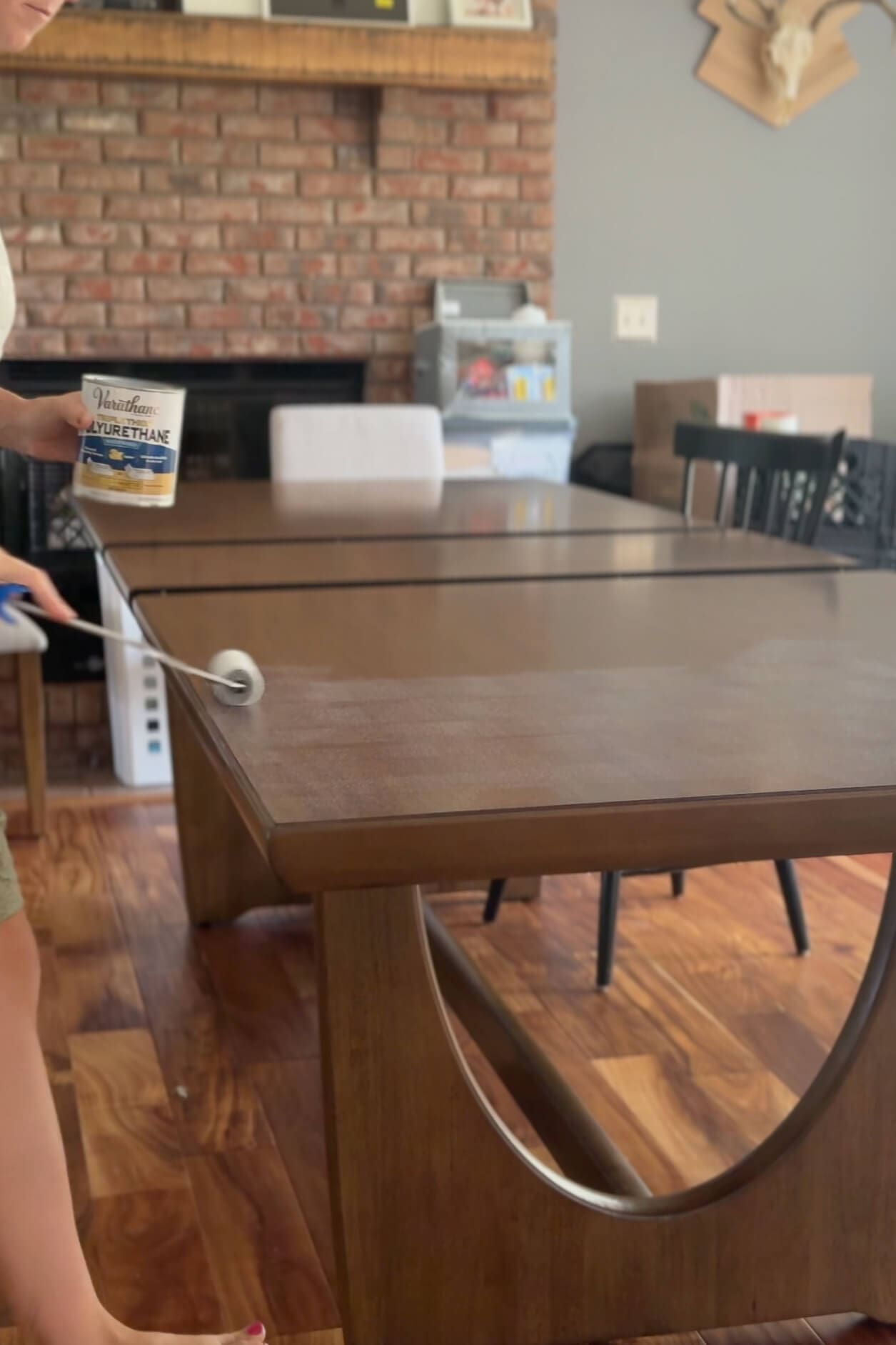 Rolling the first coat of polyurethane onto a wood dining table to protect the surface and enhance durability.