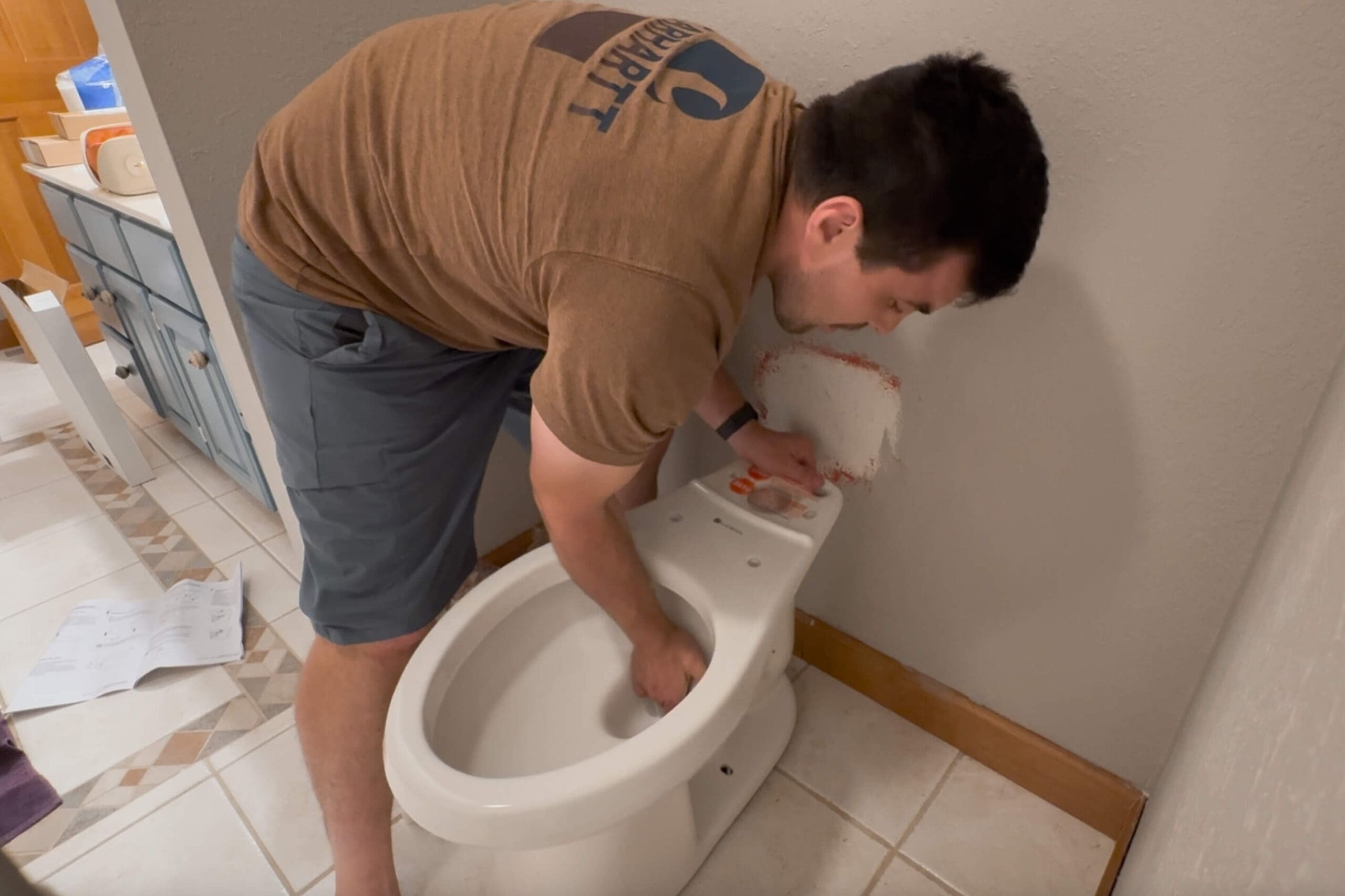 Man setting the new toilet bowl in place during a DIY project showing how to install a toilet in the primary bathroom.