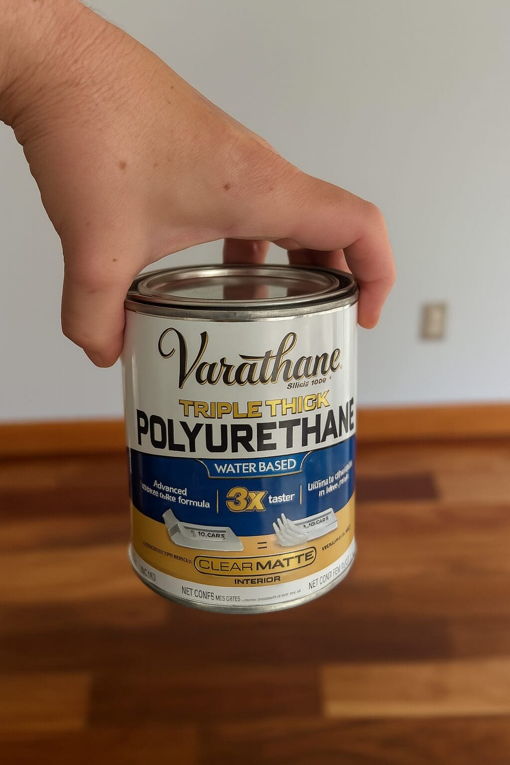 Close-up of a hand holding a can of Varathane Triple Thick Polyurethane, the water-based clear matte finish used to seal a wood dining table.