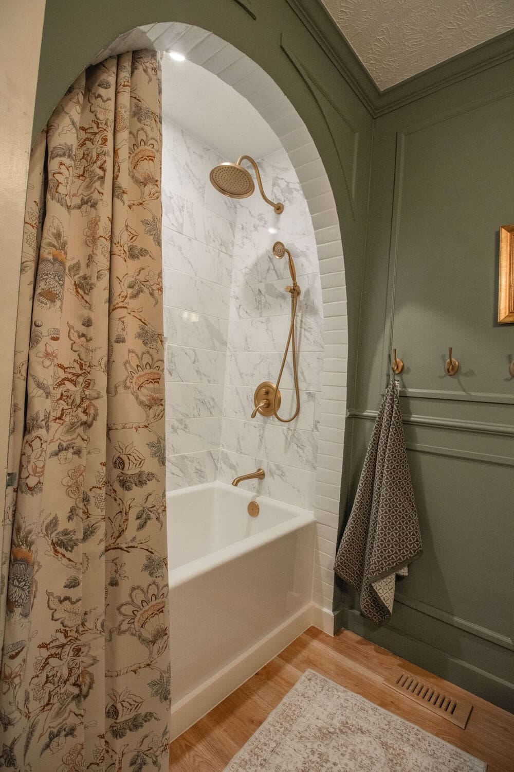Arched bathtub alcove featuring marble-look tile walls and brushed gold shower fixtures for a high-end, classic bathroom design.