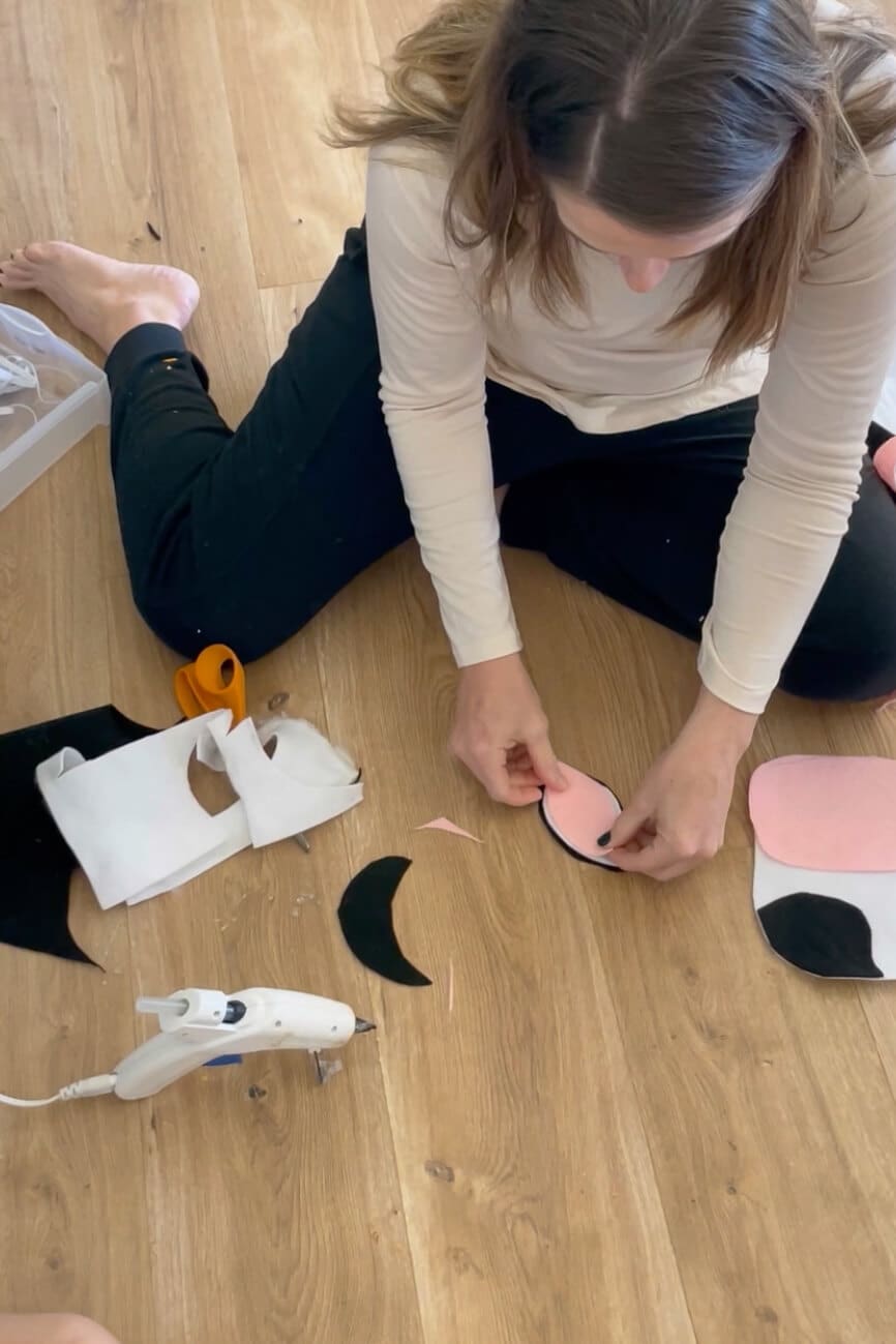 Attaching pink inner ear felt to black ear shapes while making a DIY cow costume mask.
