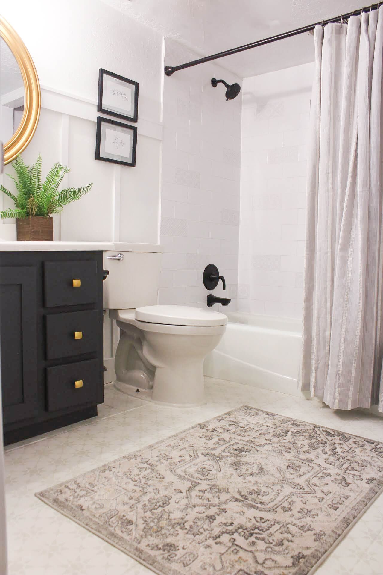 Cozy bathroom with a stenciled tile floor, black vanity with gold hardware, potted fern, round gold mirror, and black shower fixtures—styled with warm, layered decor.