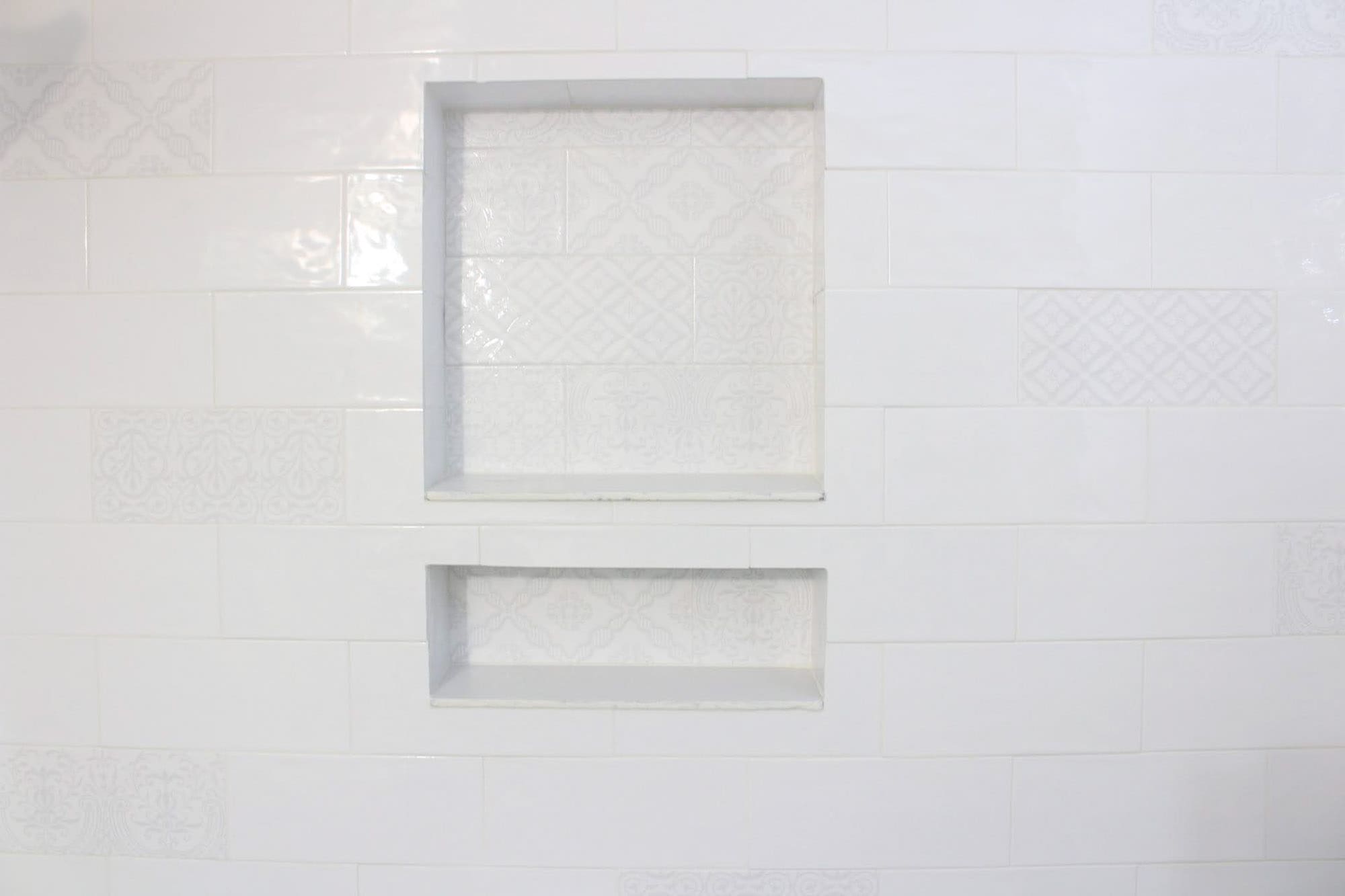 Built-in recessed double shower niches with white patterned tile backs set into a white subway tile shower wall.