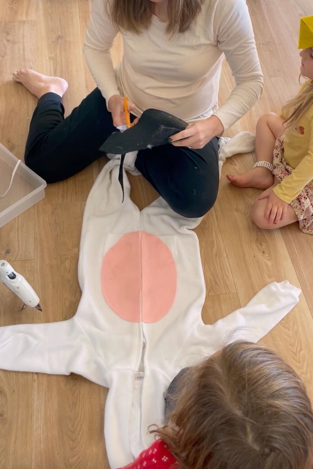 Cutting black felt spots to attach to a white jumpsuit while making a homemade Halloween costume.