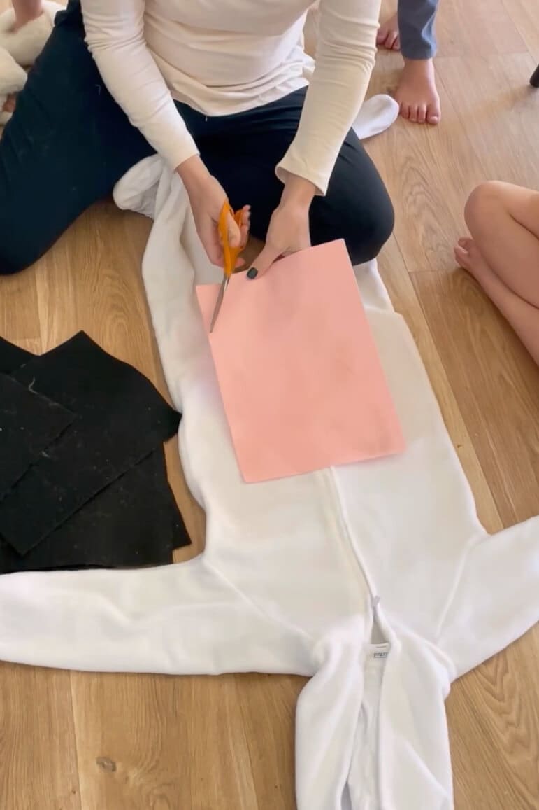Cutting pink felt for the belly patch of a homemade child's Halloween costume, with black felt spots ready to attach to the white zip-up suit.