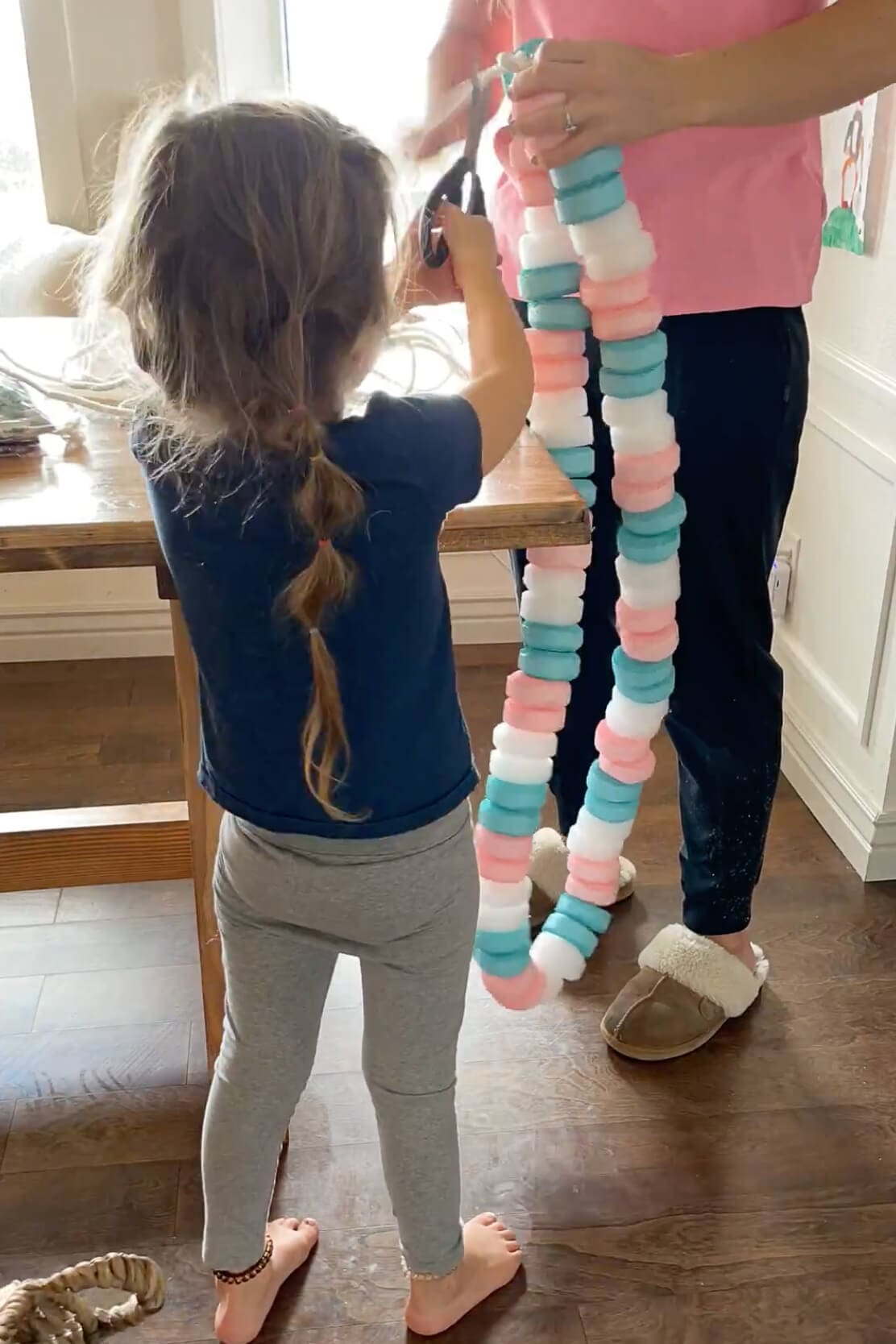 Child helping cut colorful pool noodle pieces to make a DIY candy necklace costume for Halloween.