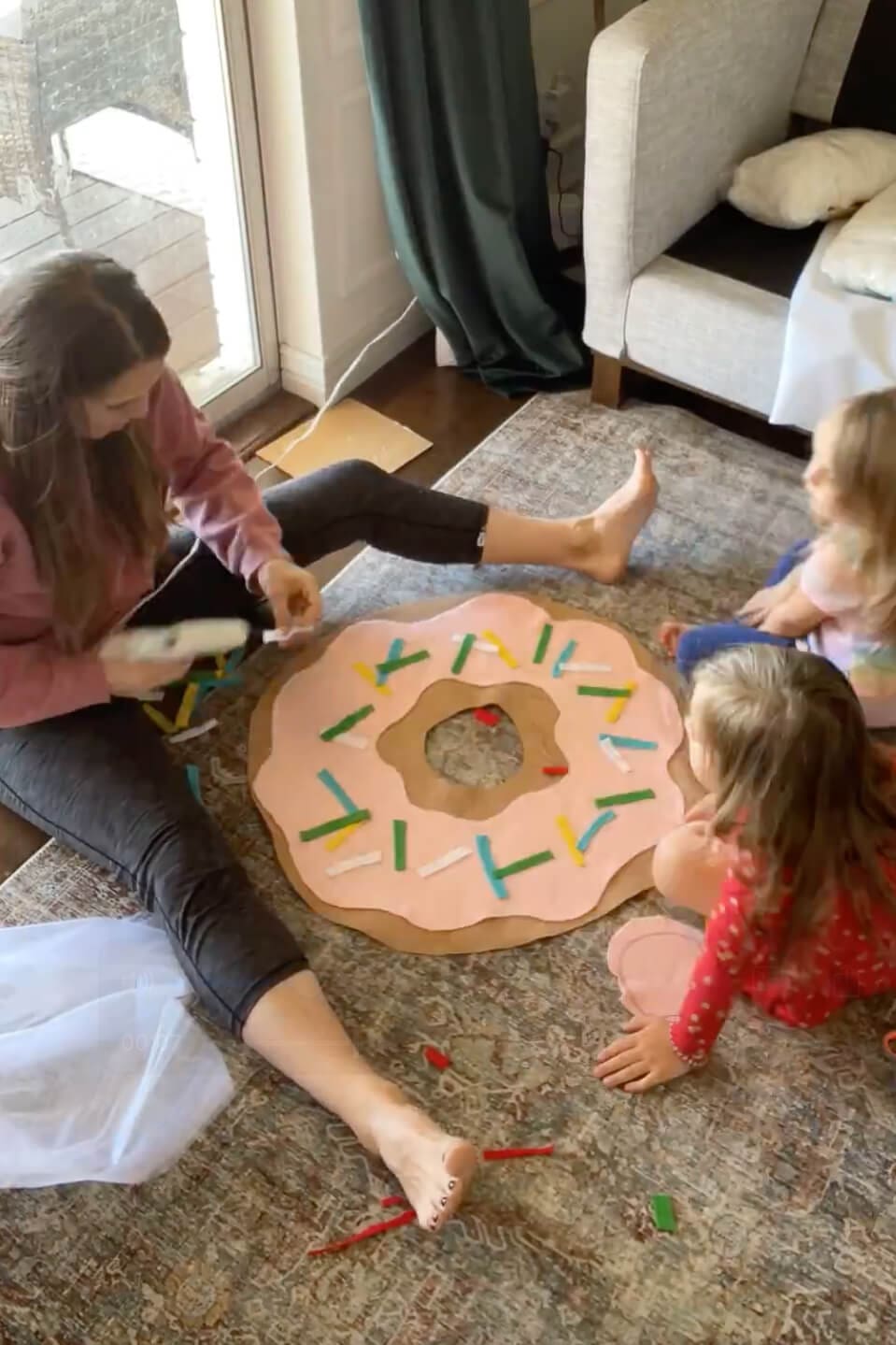 Adding colorful felt sprinkles to a pink frosted donut costume while kids help with the DIY project.