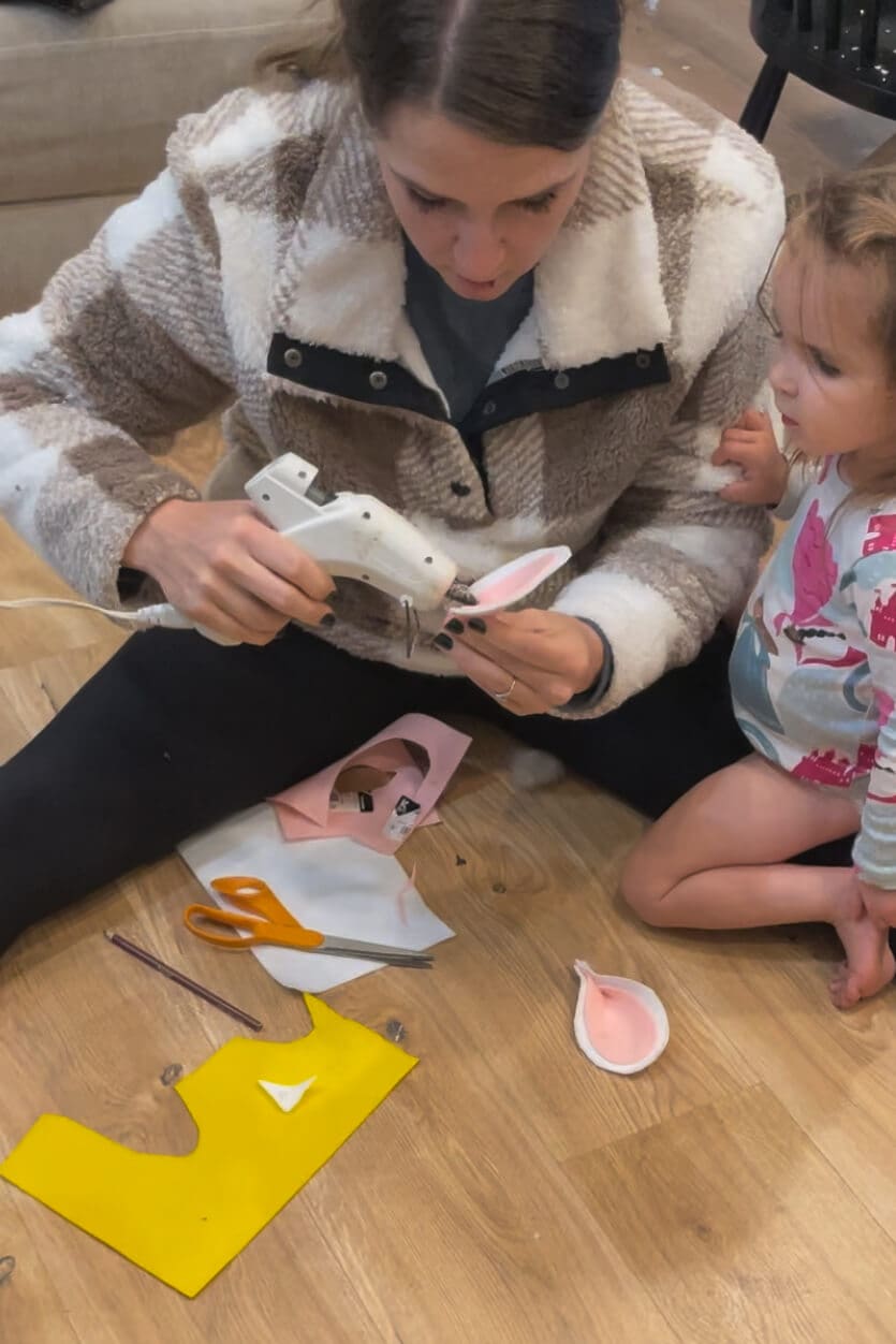 Using a hot glue gun to secure pink felt inside sheep ears while crafting a no sew sheep outfit for kids.