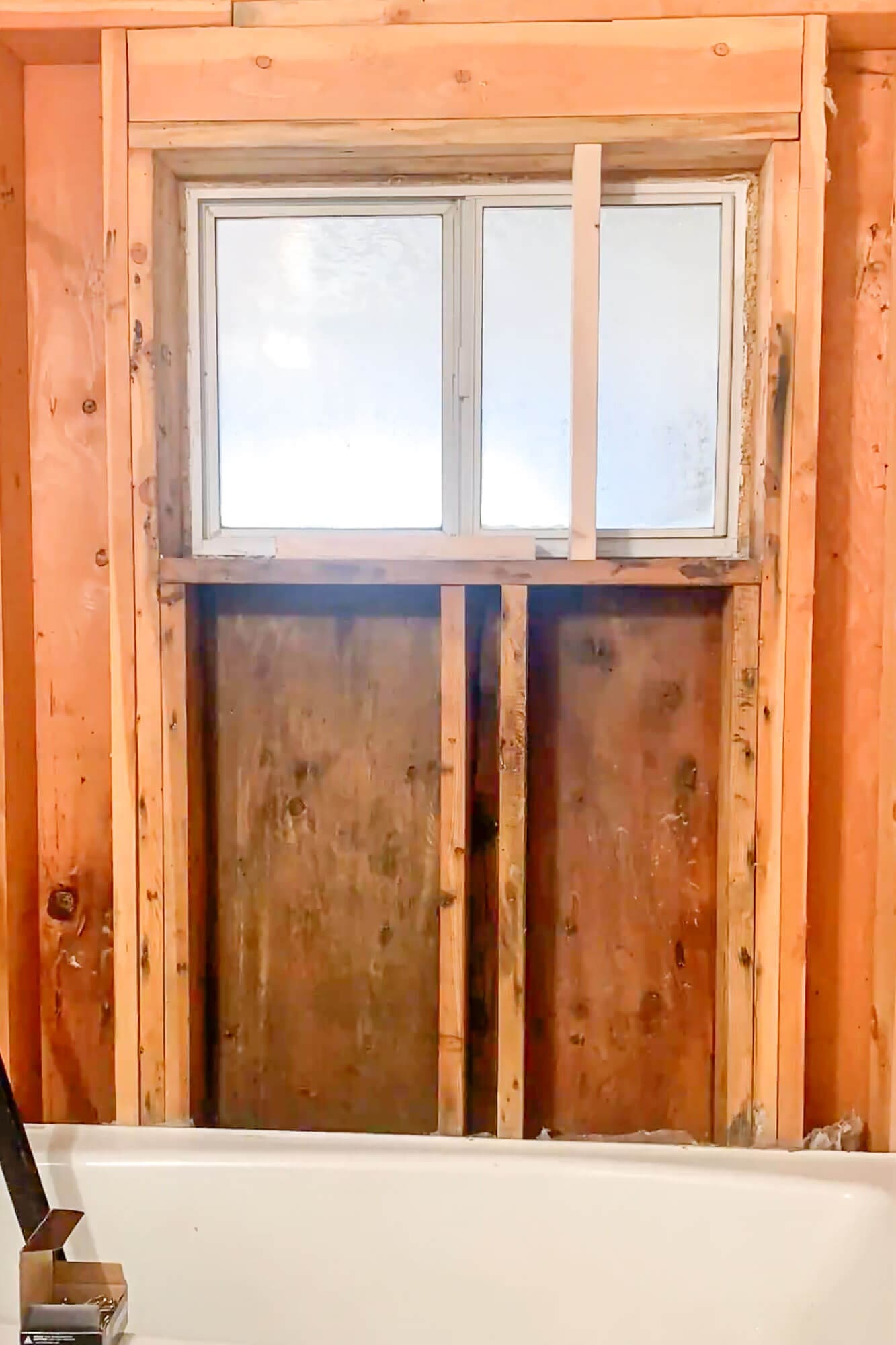 Shower wall demolition showing open wall studs and a window opening during basement bathroom remodel.